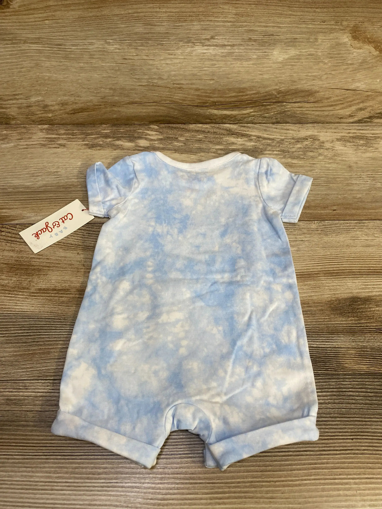 Back flat-lay of Cat & Jack romper in light blue tie-dye showing short sleeves and brand tag on wood background