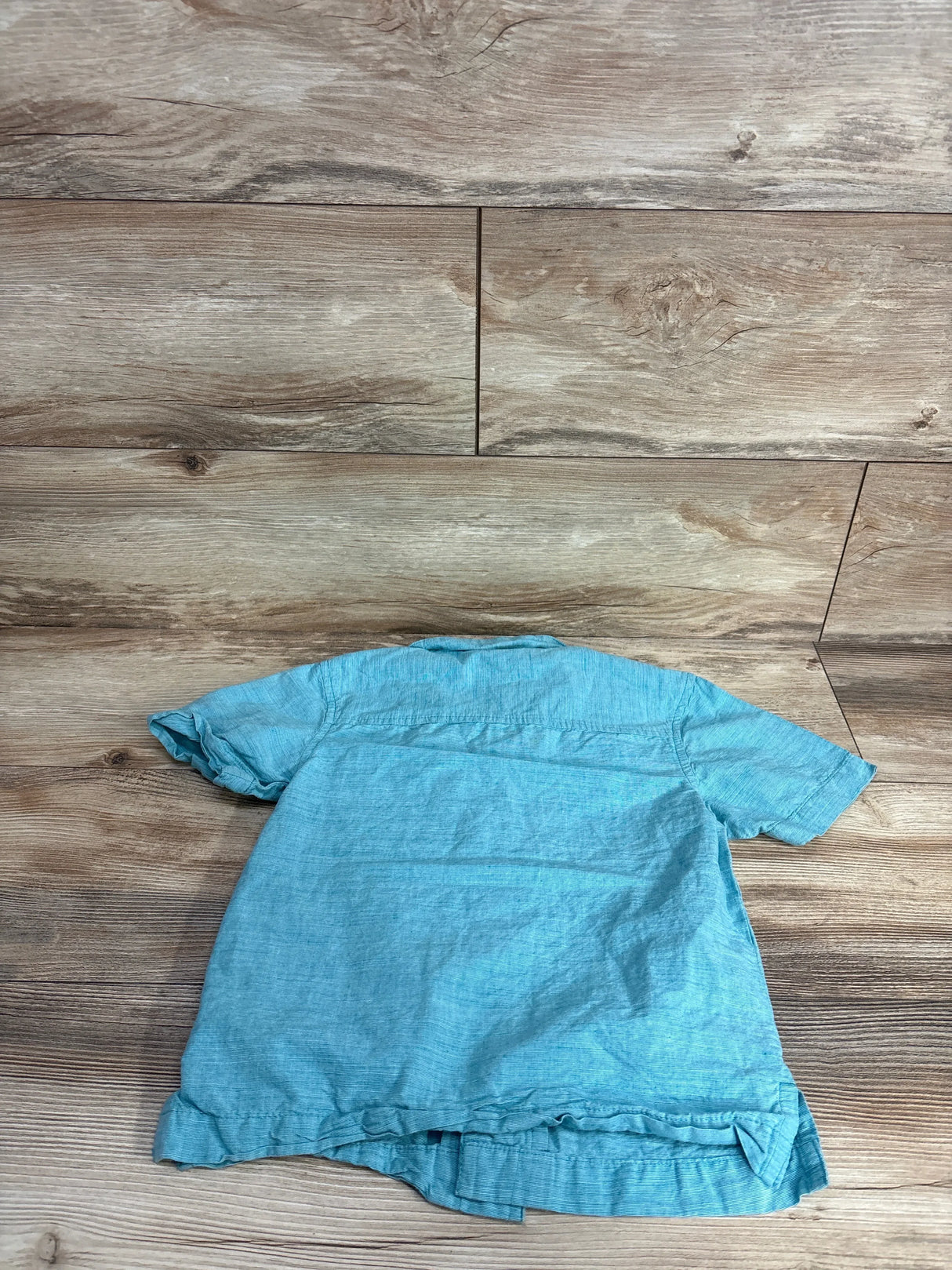 Back view of Thereabouts light blue toddler button-up shirt showing back yoke and shirttail hem on wood background