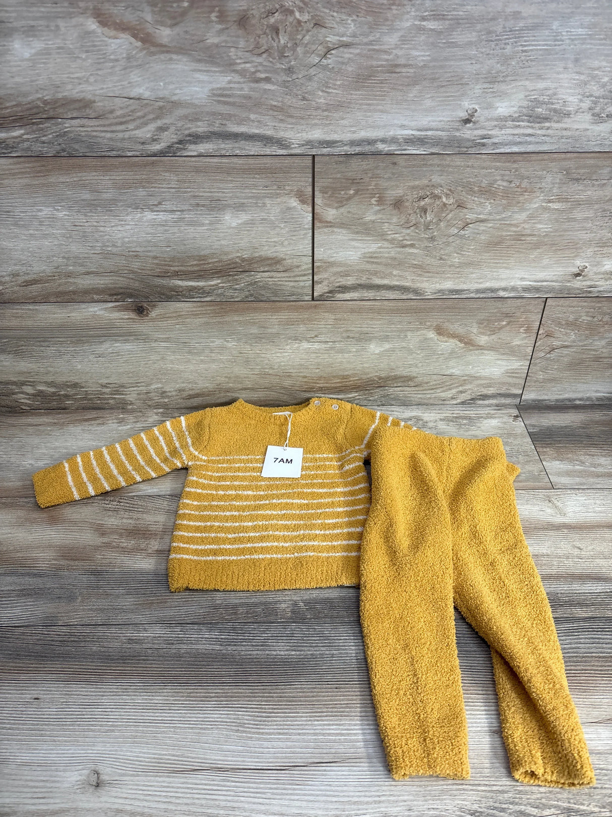 Yellow baby sweater and pants set with white stripes, laid on wood floor