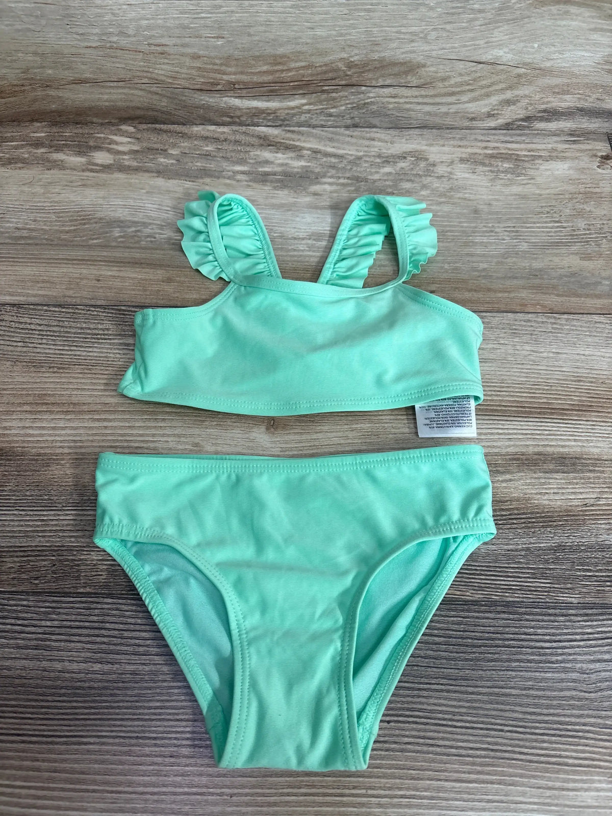 Flat lay of mint green toddler two-piece bikini showing ruffle-trimmed shoulder straps and matching briefs on wood background