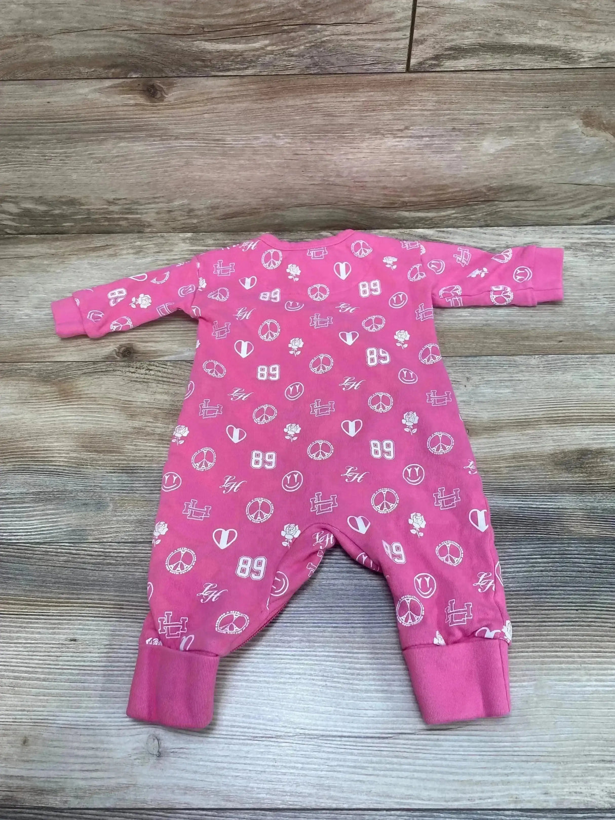 Flat lay of Lil Homme pink one piece romper showing all over peace sign, heart, rose and 89 prints on wooden floor background