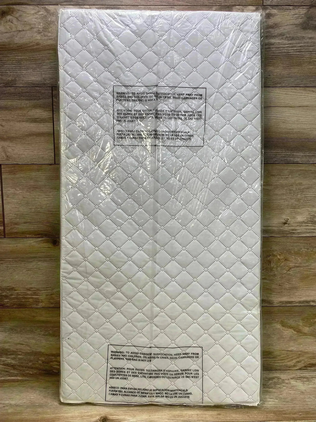Top-down view of Dream On Me cradle mattress showcasing quilted white surface and plastic packaging on wood floor, 36 by 18 by 2 inches