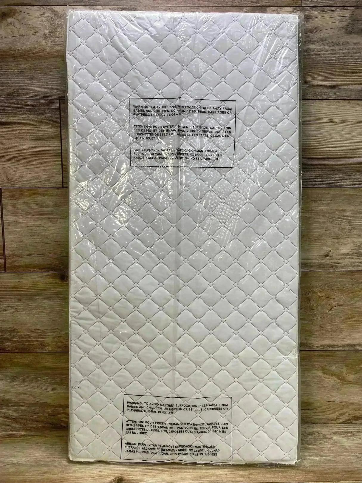 Top-down view of Dream On Me cradle mattress showcasing quilted white surface and plastic packaging on wood floor, 36 by 18 by 2 inches