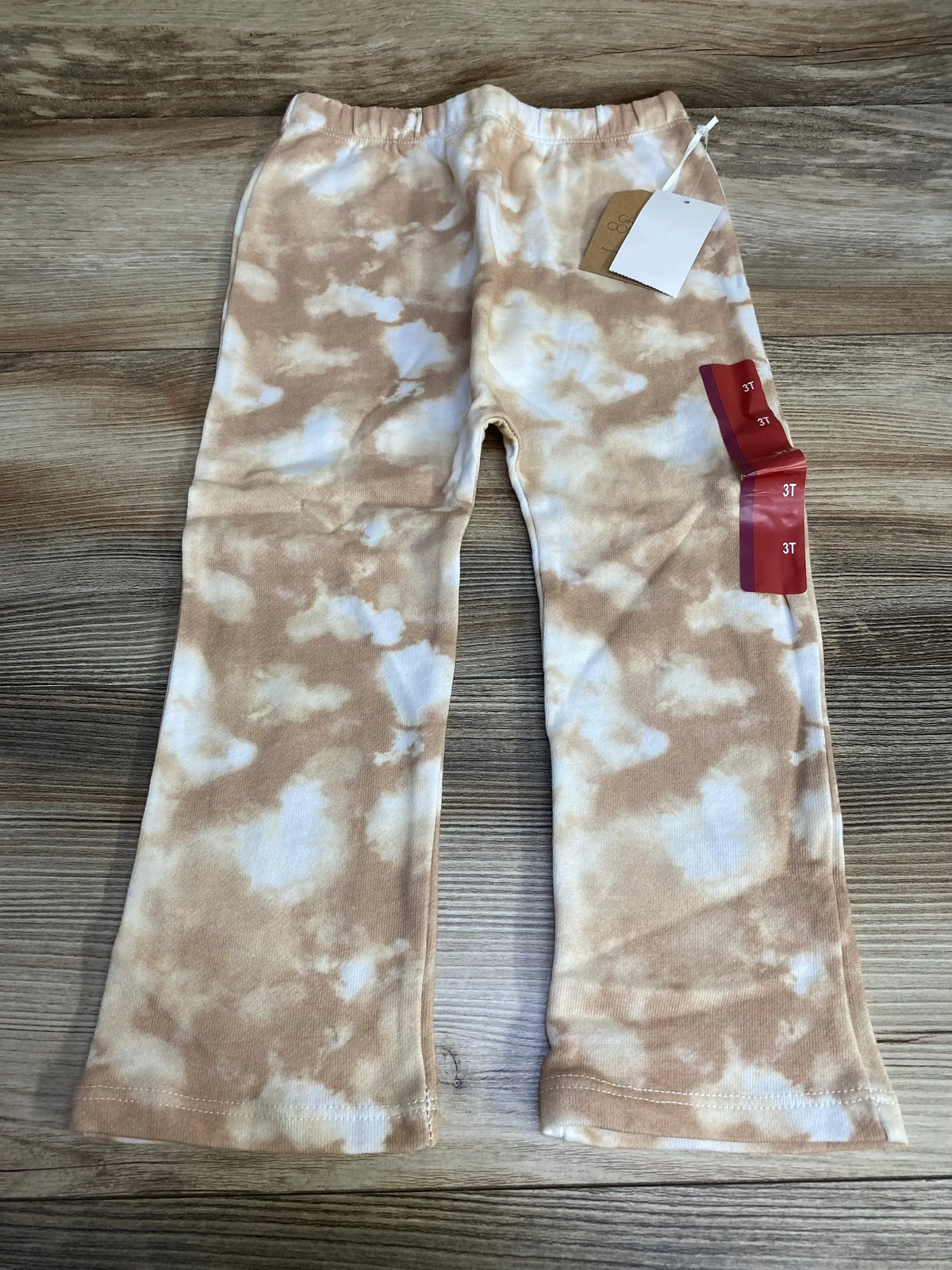 Flat lay of Grayson Collective toddler tie-dye pants, brown and white, showing elastic waistband and visible 3T size tag on wood background