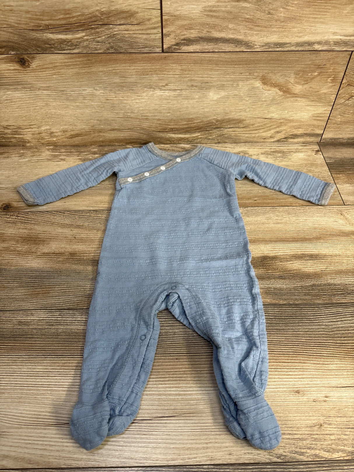 Blue long sleeve baby footed romper with buttons on wooden floor