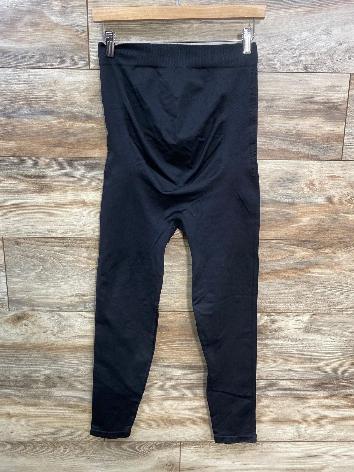 Black high-waisted maternity leggings hanging on wooden hanger, wood floor background