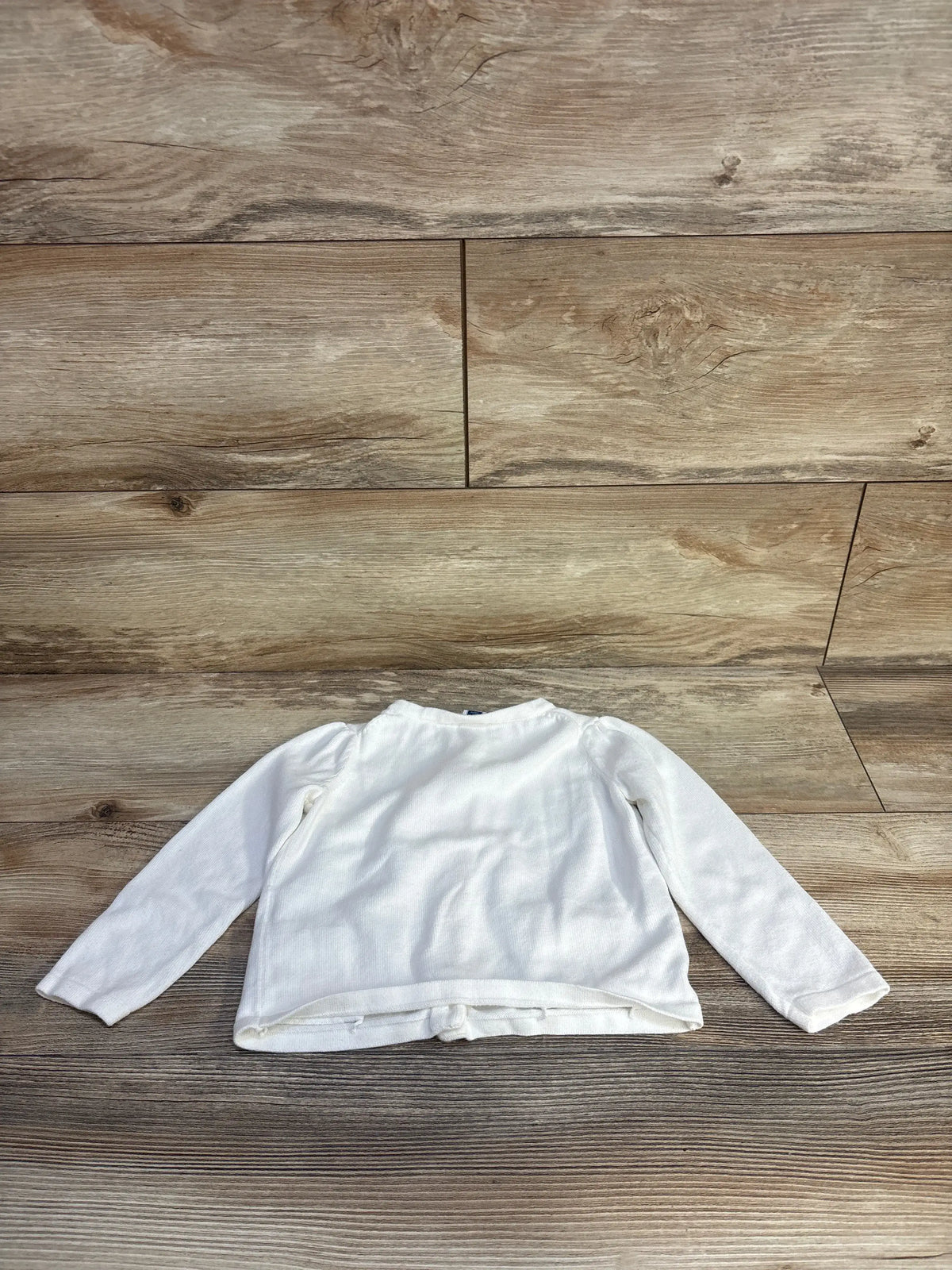 Back view of white Janie and Jack bow pocket cardigan showing long sleeves on a wood floor