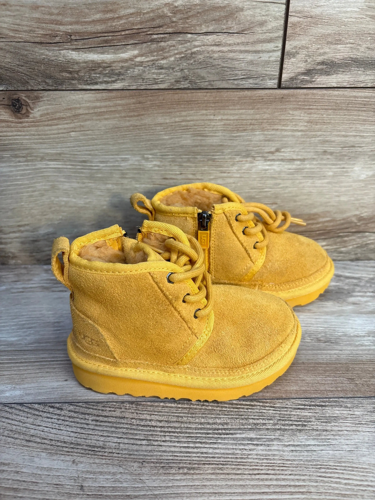 Three-quarter view of NWOT Ugg Neumel II boots in yellow suede size 8c showcasing lace-up front side zip and fur lining on wood plank floor