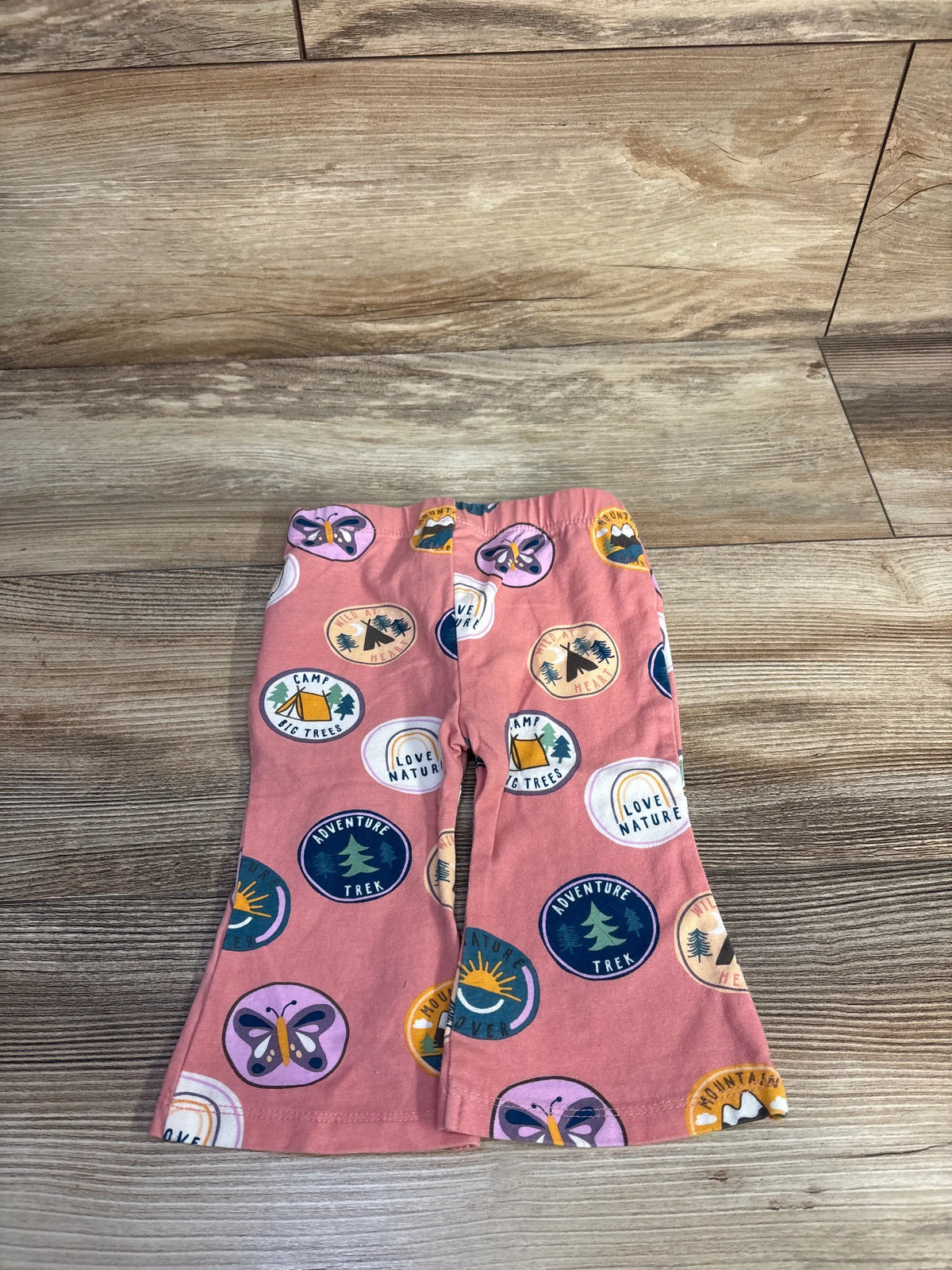 Front view of Cotton On Baby pink flared leggings showcasing colorful camping and butterfly print on a wood floor