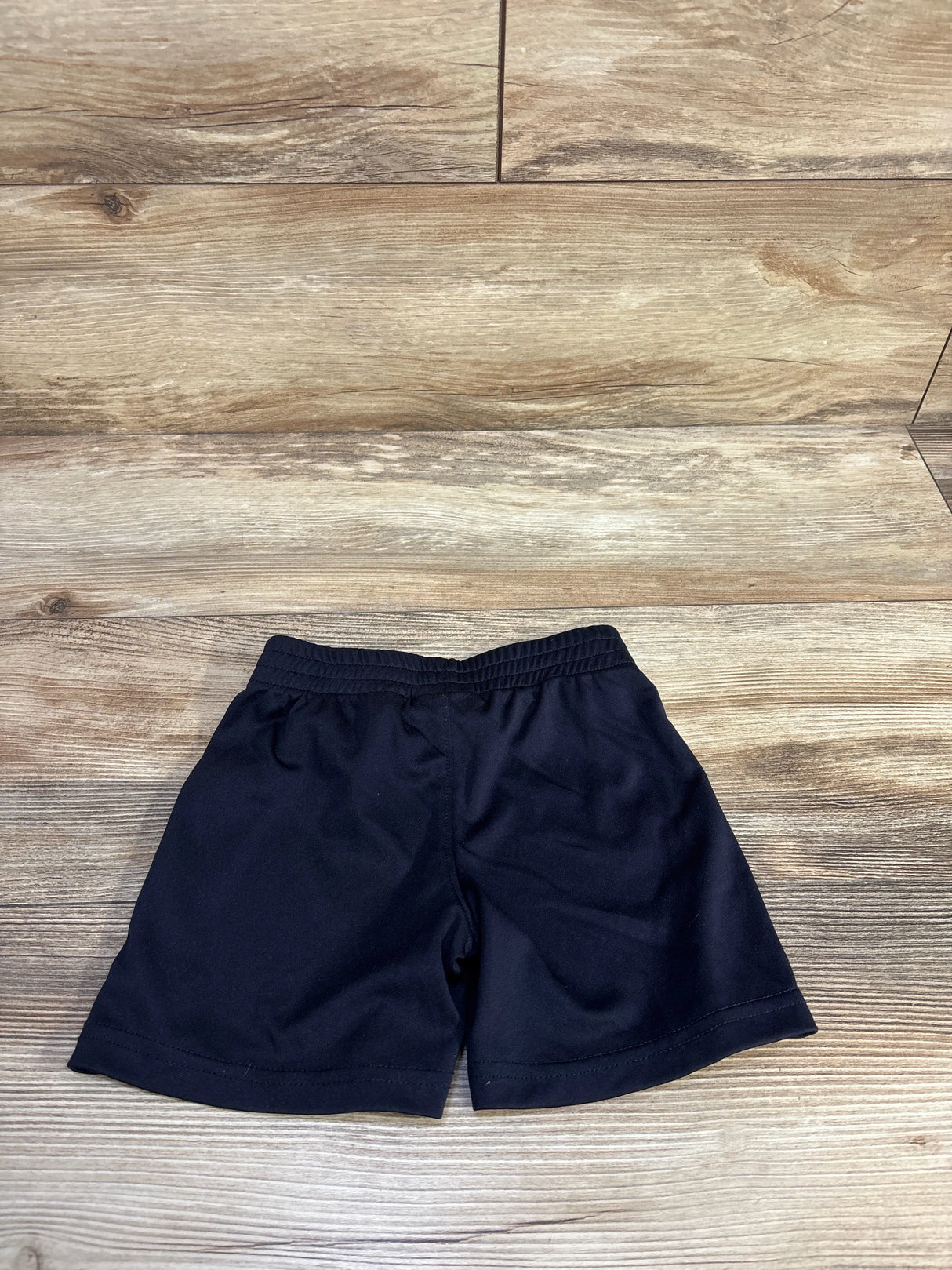 Flat lay of black Puma toddler active shorts showcasing elastic waistband and knee-length cut with light wood background