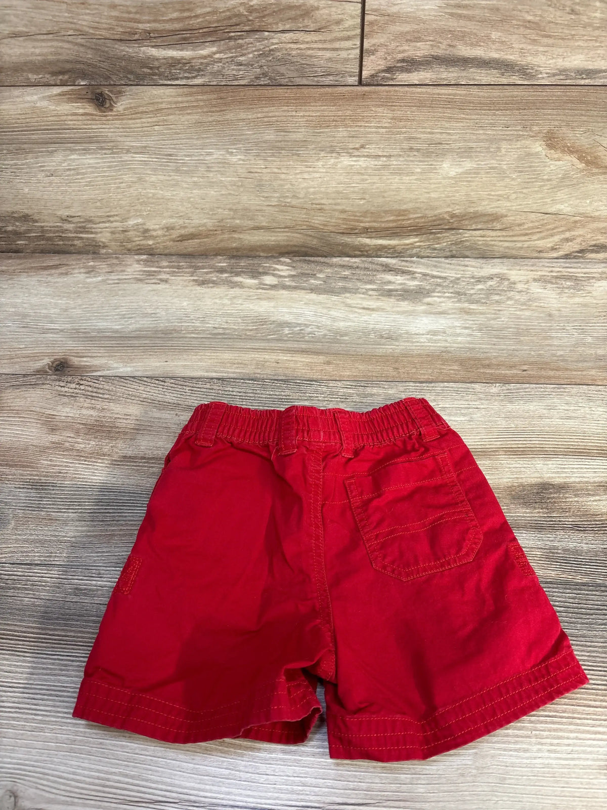 Flat-lay back view of red Ralph Lauren toddler shorts showing elastic waistband and back patch pocket on wood floor background