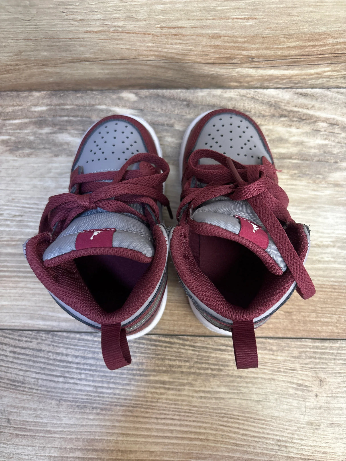 Top-down view of Air Jordan 1 Mid TD Cherrywood Red toddler sneakers showcasing maroon and gray upper, padded collar and laces on wooden floor