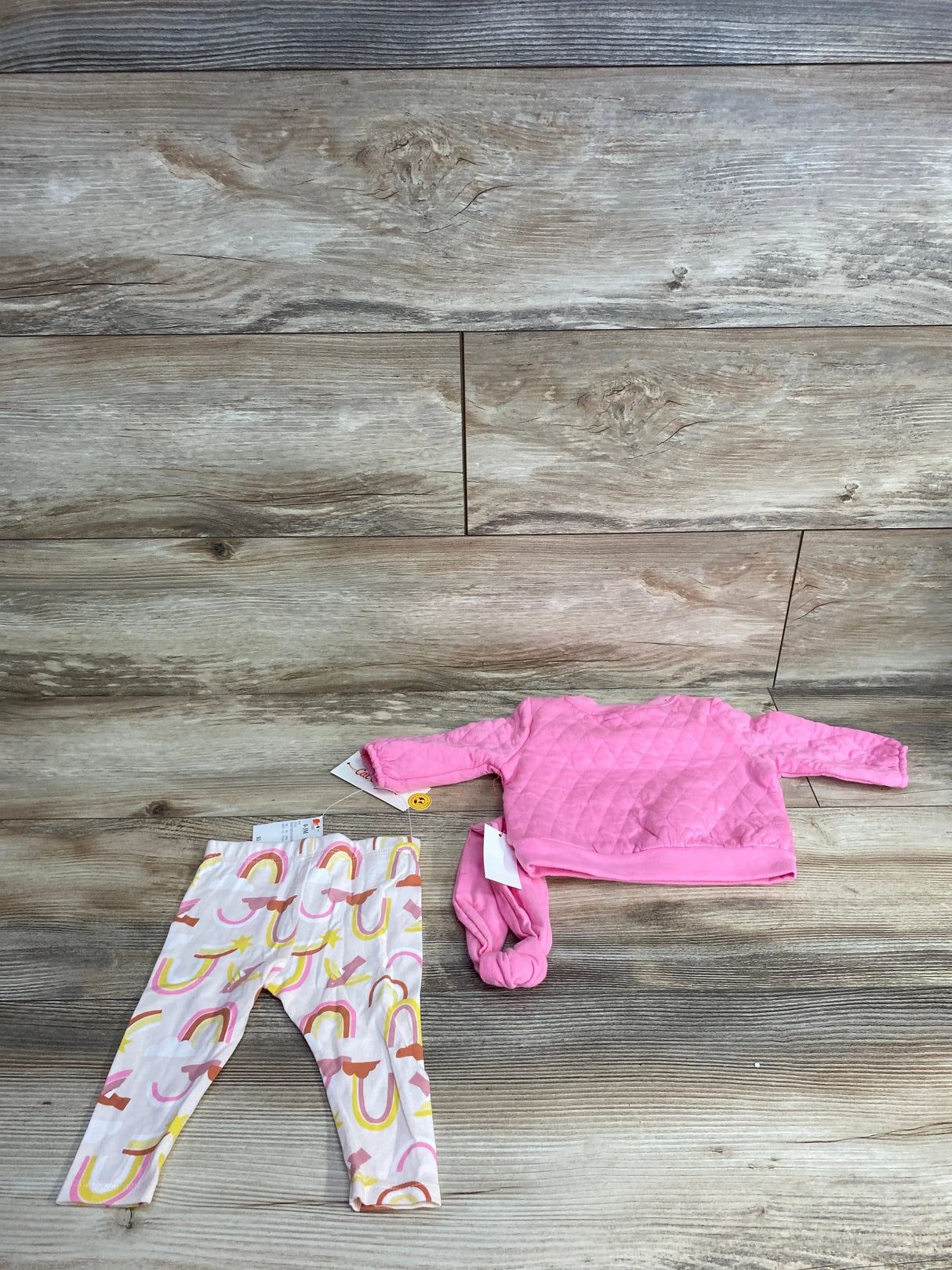 Baby girl outfit with pink quilted long sleeve top, rainbow print leggings, and matching headband on wood background