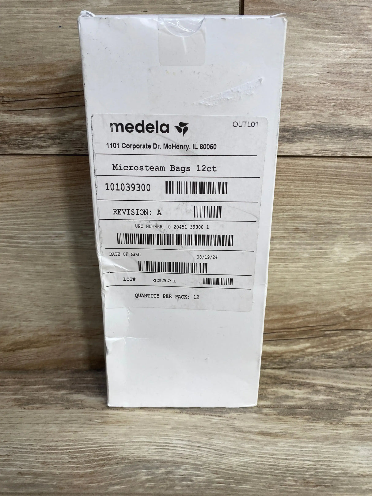 Front view of Medela Quick Clean Micro Steam Bags box showing label with Microsteam Bags 12ct and lot/date on wood background