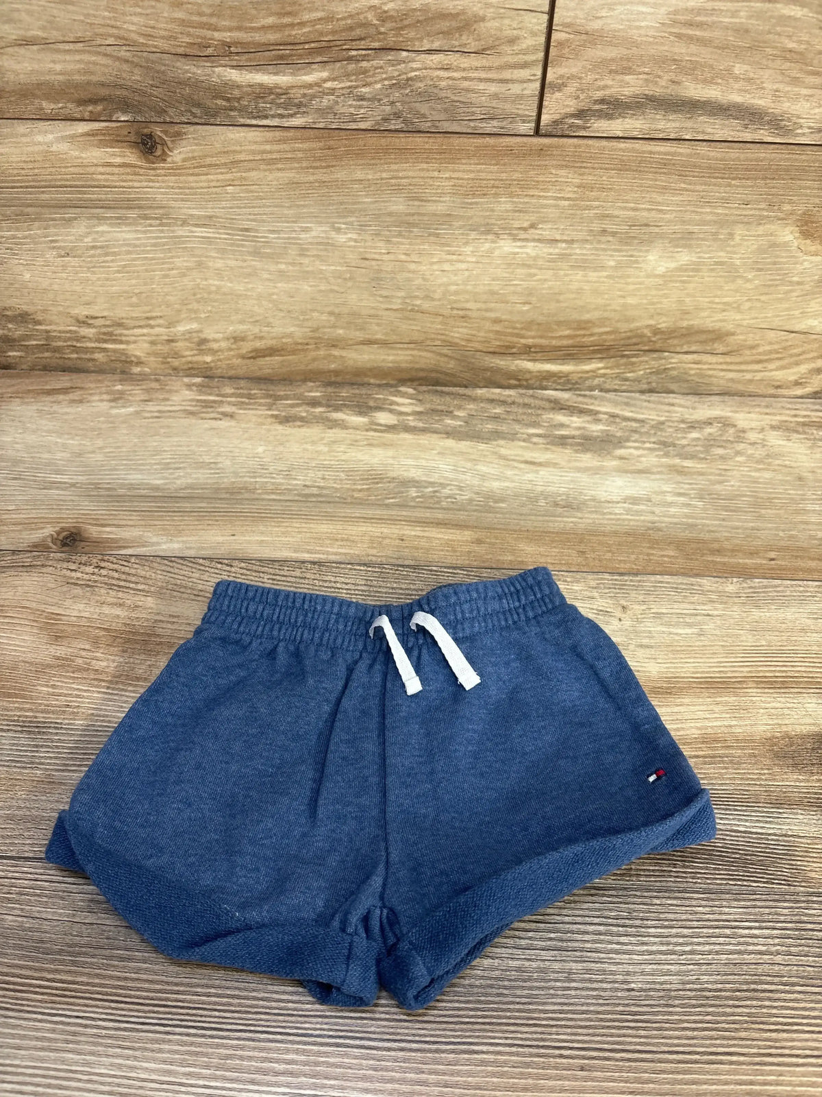 Flat lay of toddler blue Tommy Hilfiger pull-on shorts showcasing elastic drawstring waistband and rolled cuffs on wood floor