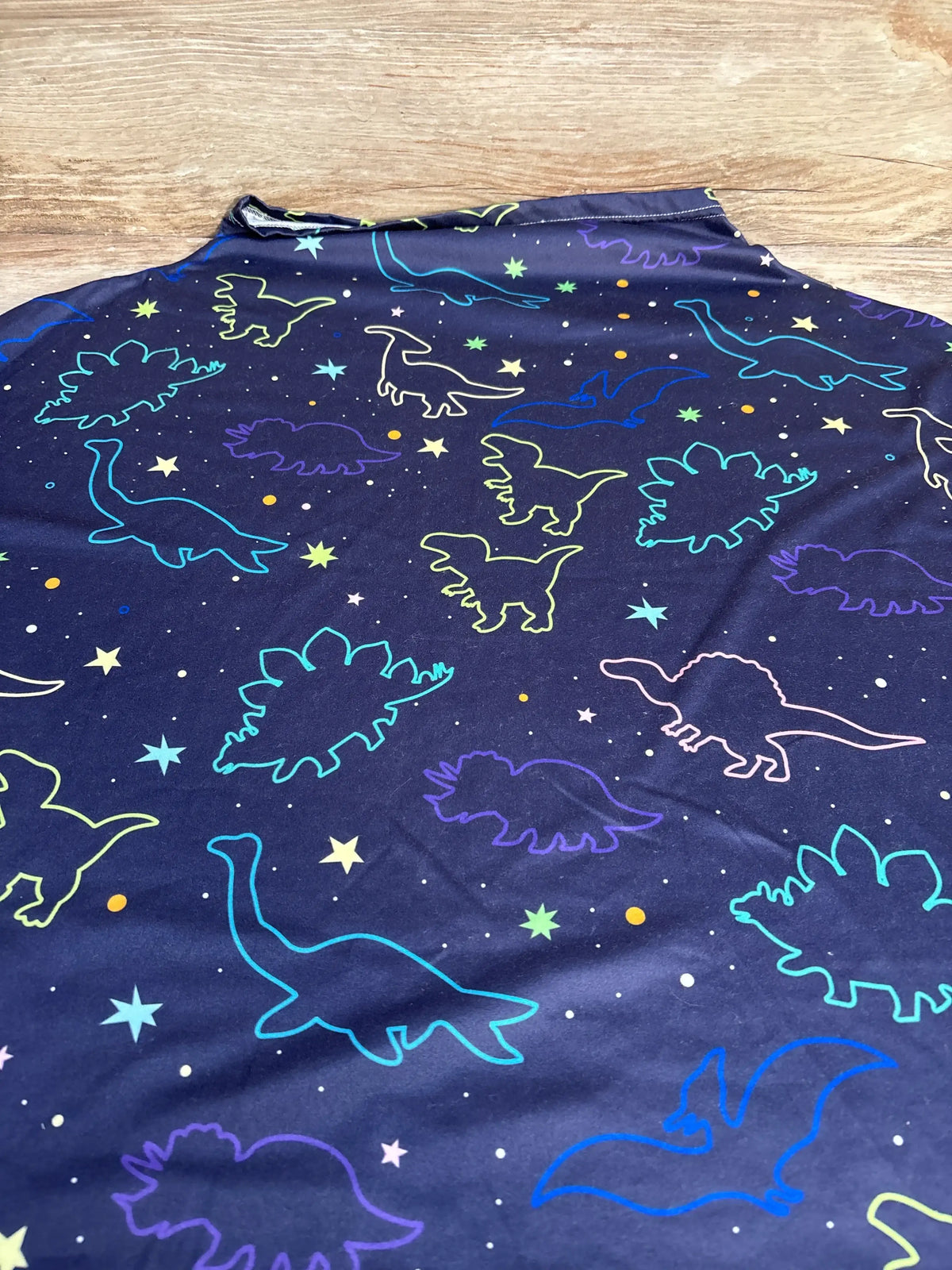 Close-up of navy dinosaur print multi-use nursing and car seat cover with colorful dinosaur outlines on a wooden surface