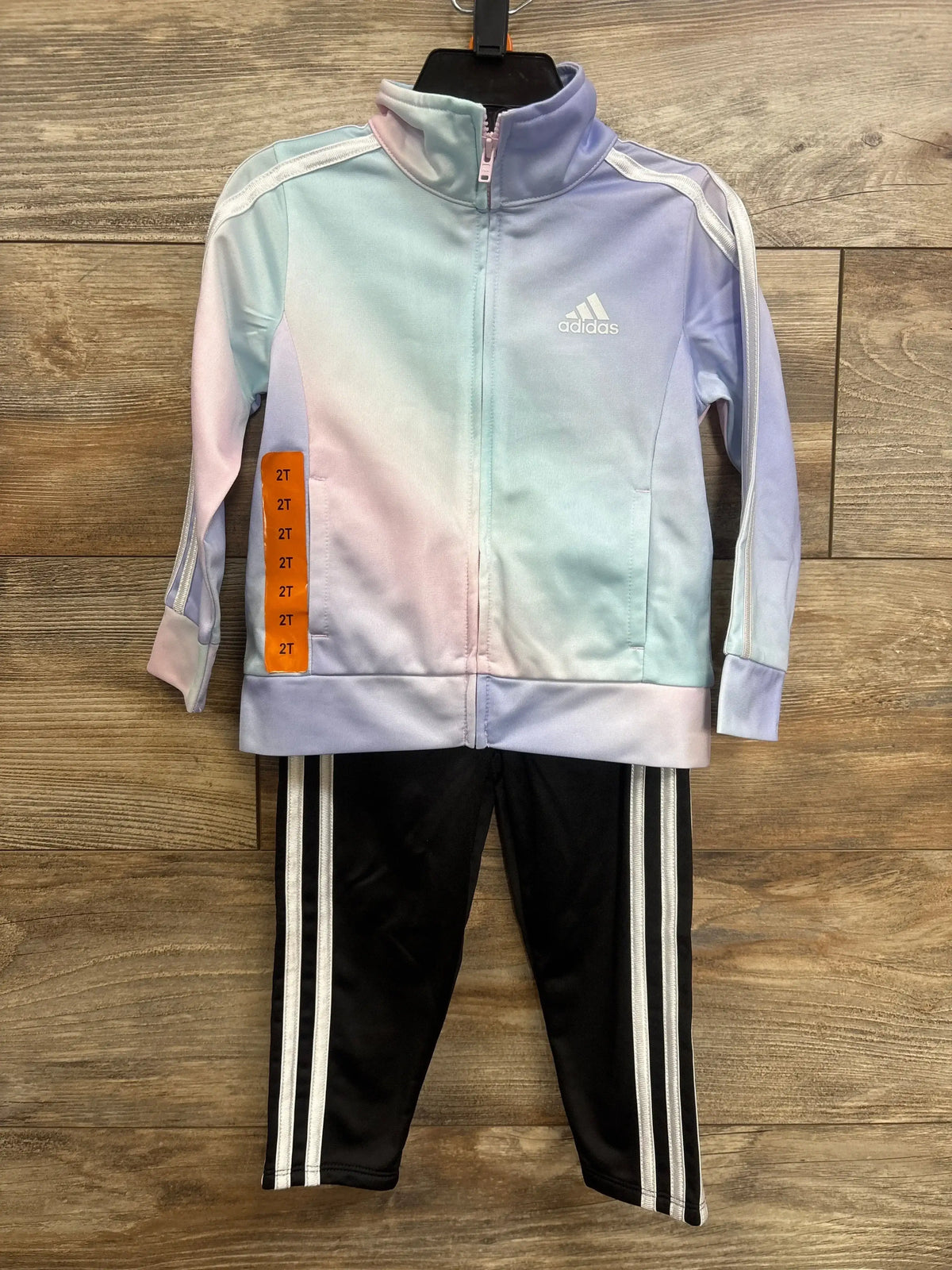 Front view of toddler Adidas tracksuit size 2T: pastel ombre zip jacket with white logo; black pants with white stripes