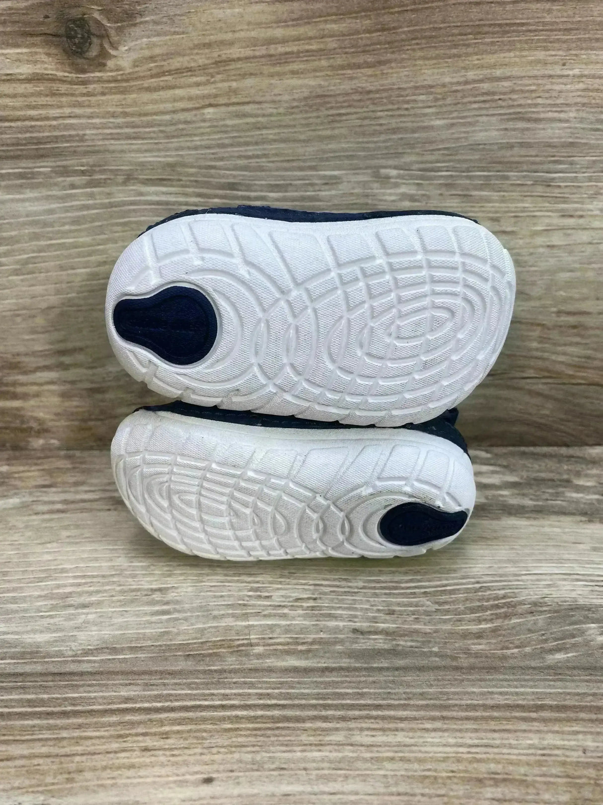 Bottom view of Stride Rite Jamie toddler sneakers showing white textured outsoles and navy uppers, size 3C, on wood background
