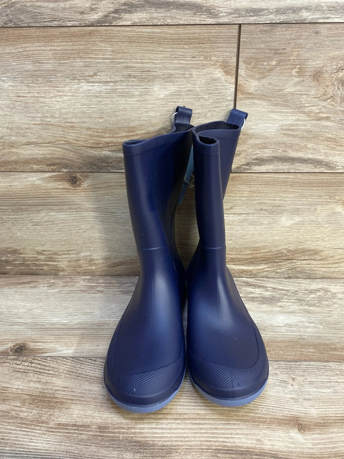 Front view of Cat and Jack navy rain boots size 4Y showing tall rubber shaft, textured toe and pull tabs on wood background