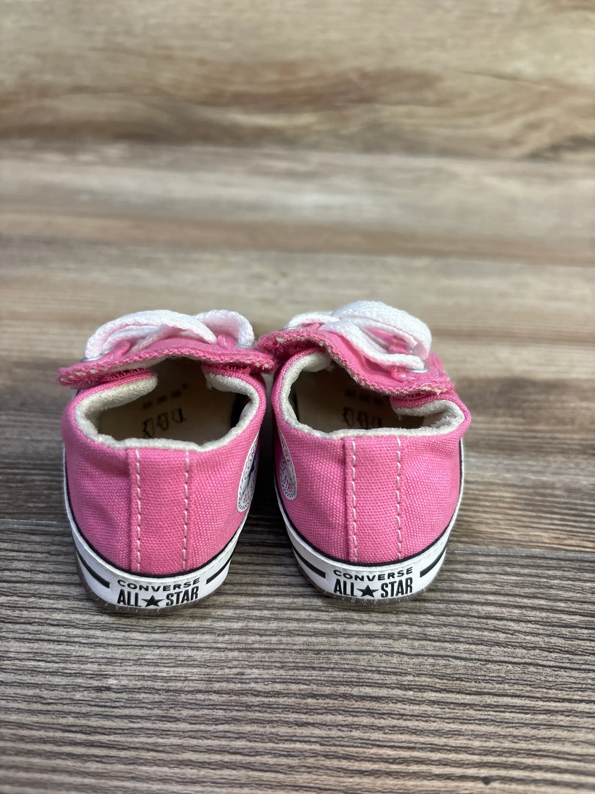 Rear view of pink Converse Cribster shoes showing CONVERSE ALL STAR heel logo and Velcro straps on wood floor