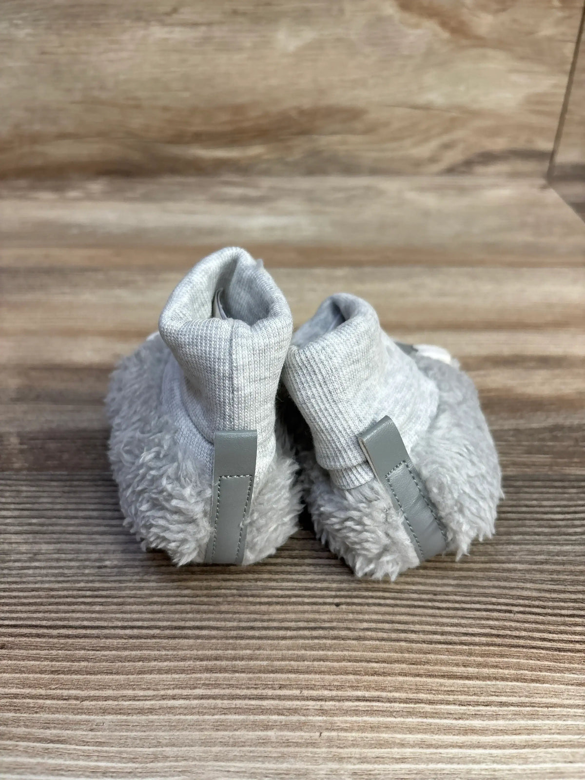 Pair of gray fuzzy baby booties with soft fabric cuffs on wooden surface