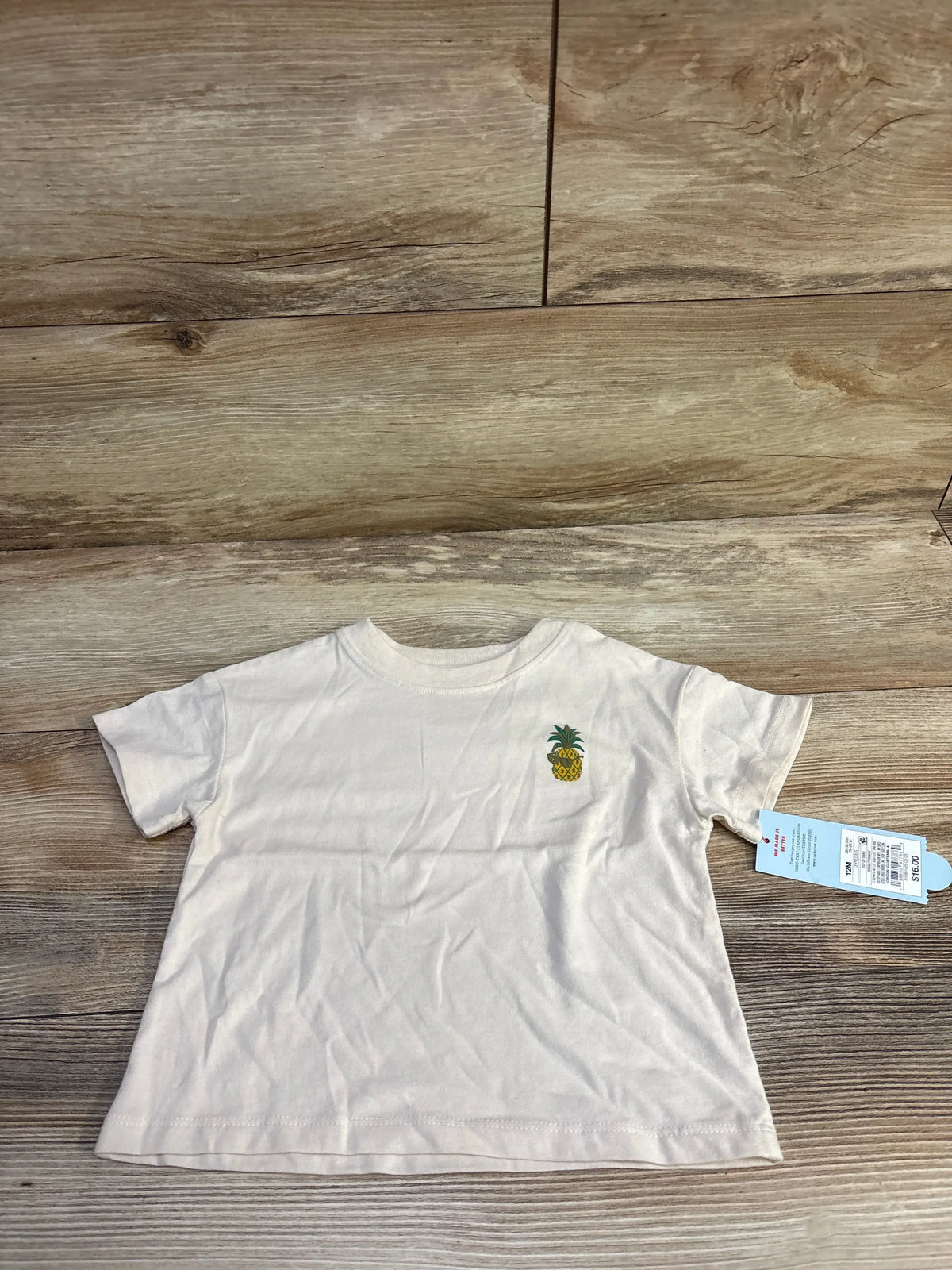 Flat lay of Cat & Jack beige 12-month short-sleeve t-shirt showcasing small pineapple chest graphic on wood background