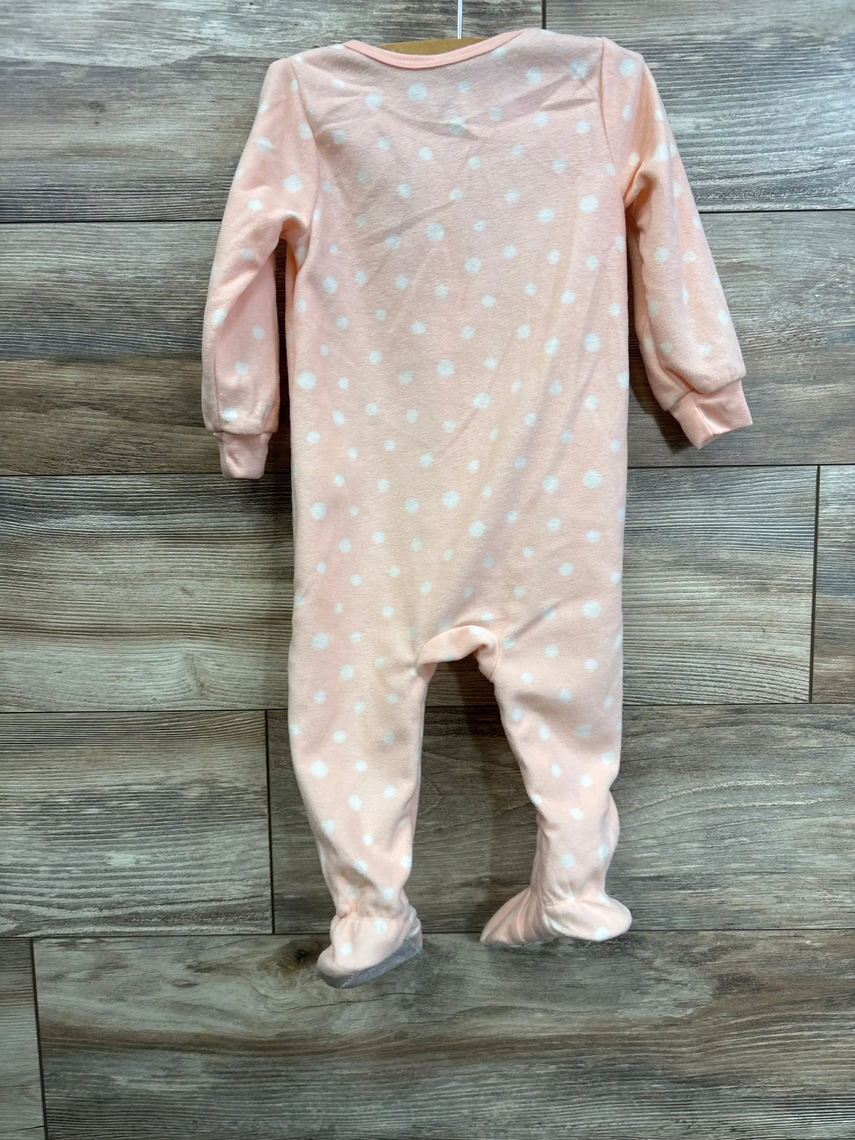 Back view of Kids Headquarters footed blanket sleeper showing pink fabric with white polka dots, long sleeves, and enclosed feet on a wooden plank background