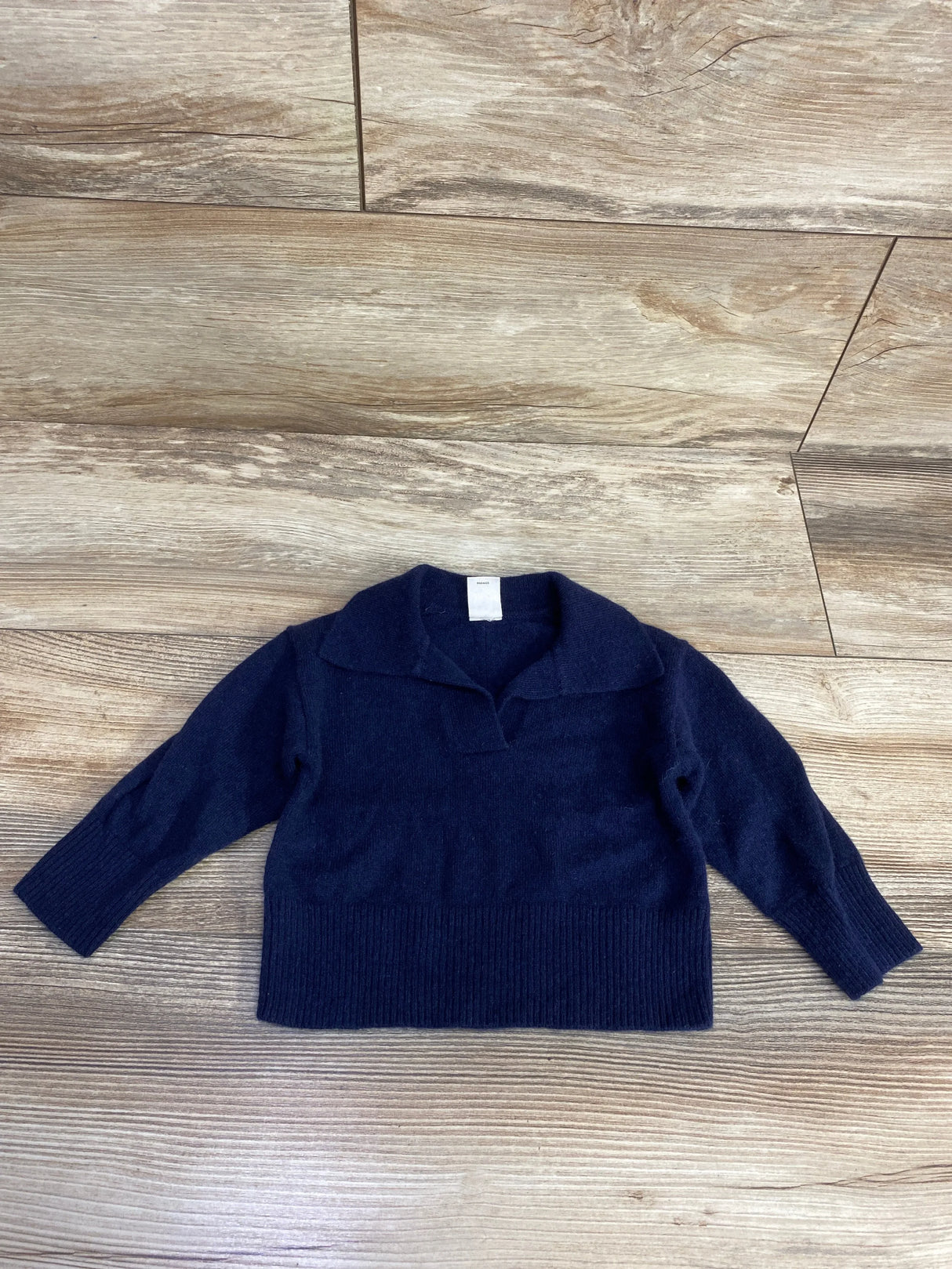 Navy blue long sleeve toddler sweater with collar, laid flat on wooden floor