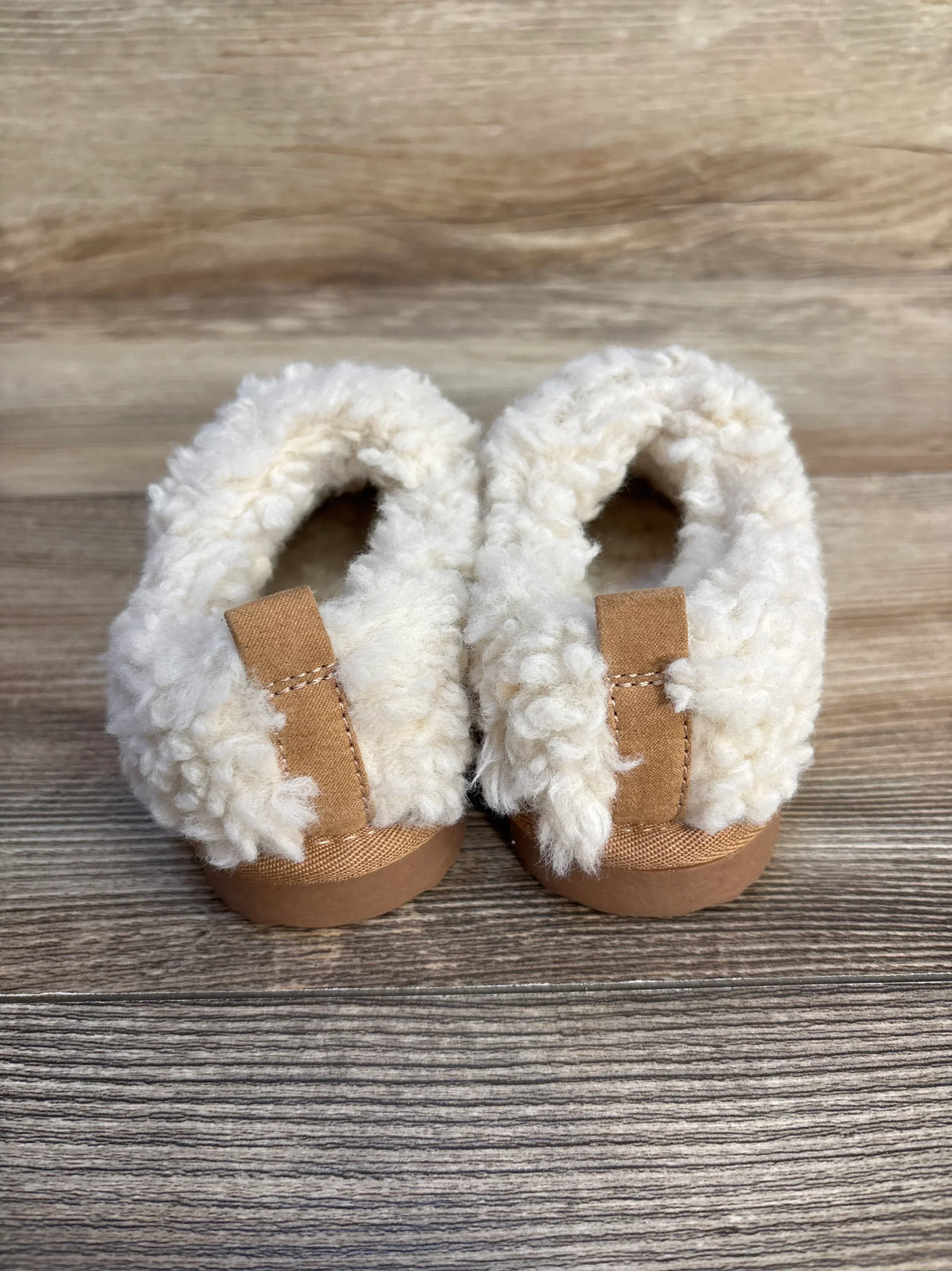 Back view of cozy infant shearling slippers with tan soles on wood background