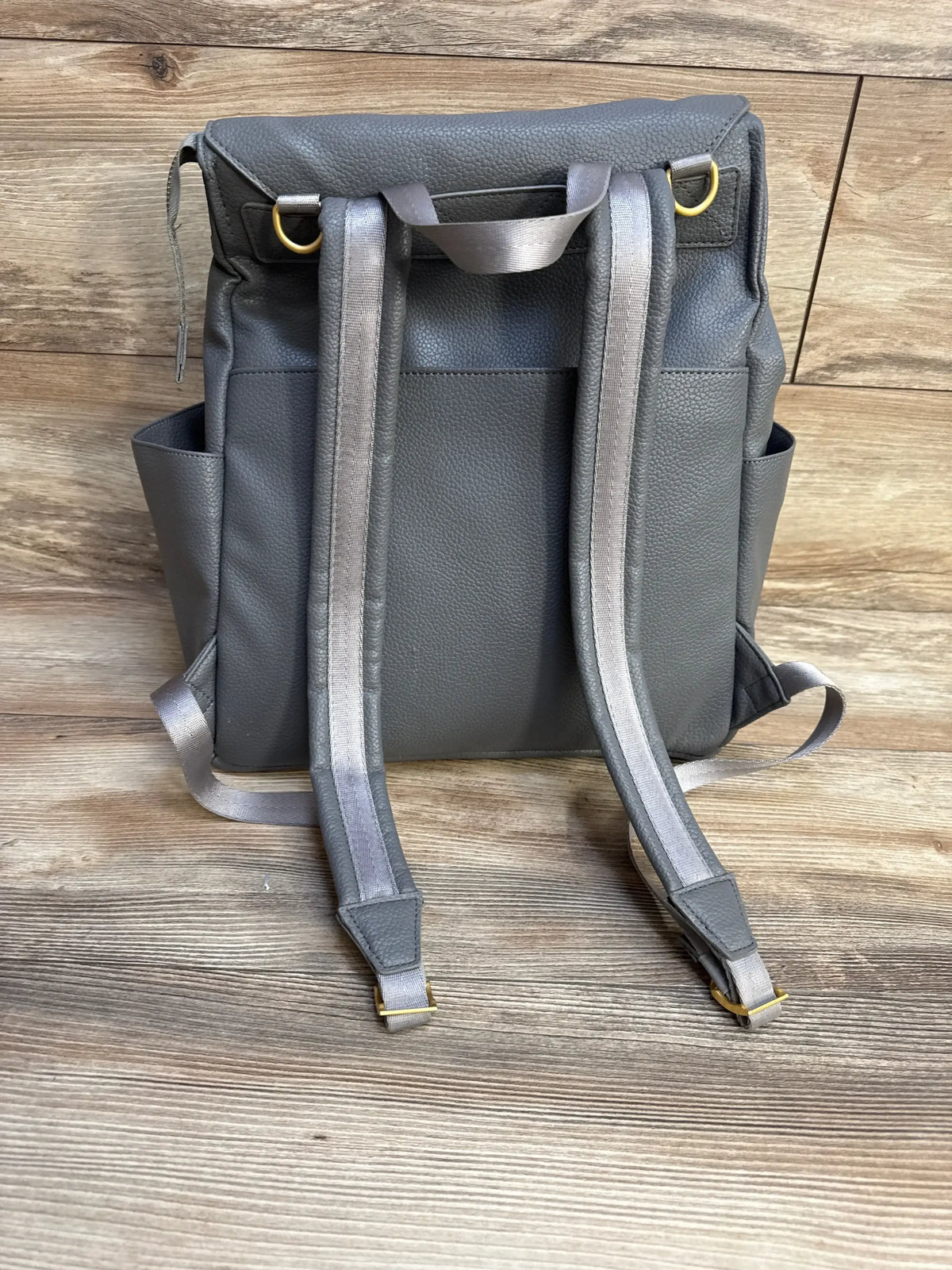 Back of Freshly Picked Stone Classic Diaper Bag II with padded straps, top carry handle and side pockets on wood background