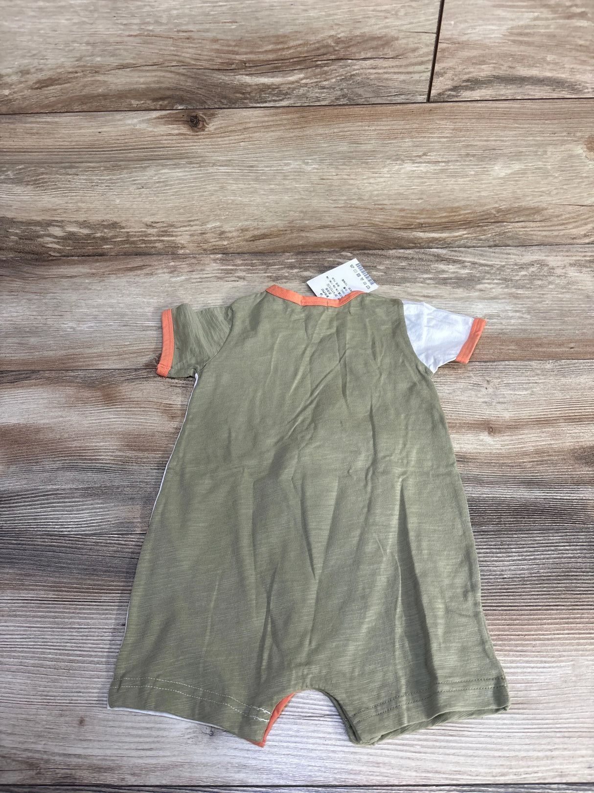 Back view of Chic a Bon shortie romper, olive green with one white sleeve and orange trim, on wood background