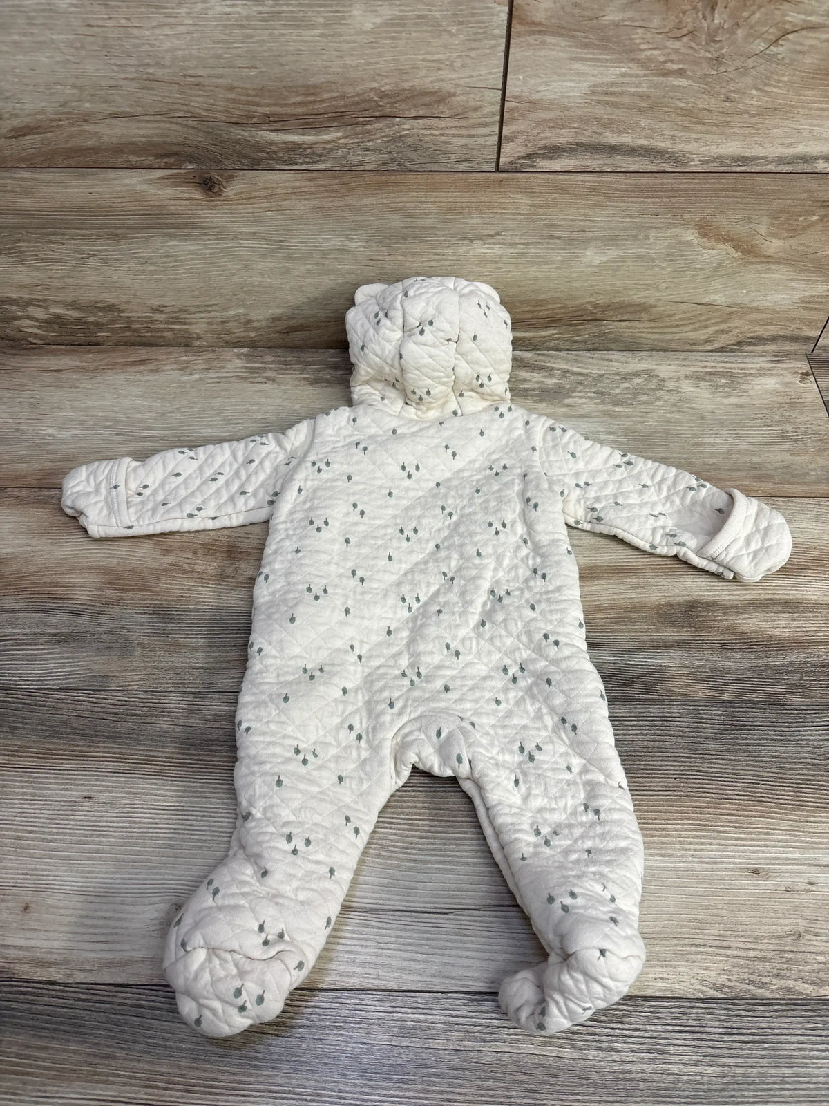White quilted baby snowsuit with hood and small gray tree pattern on wooden floor