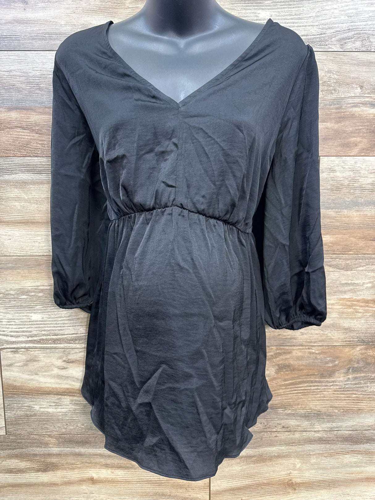 Black maternity blouse with V-neck and elastic waist on mannequin against wooden background