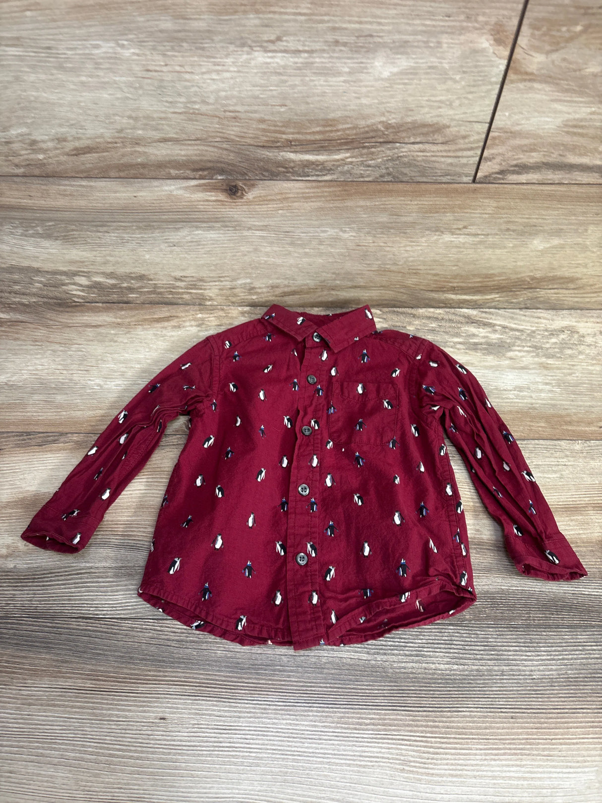 Burgundy long sleeve kids button-up shirt with penguin print on wood background