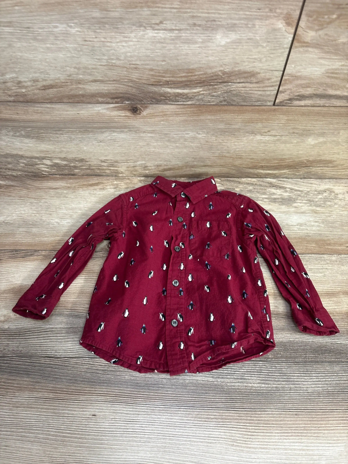 Burgundy long sleeve kids button-up shirt with penguin print on wood background
