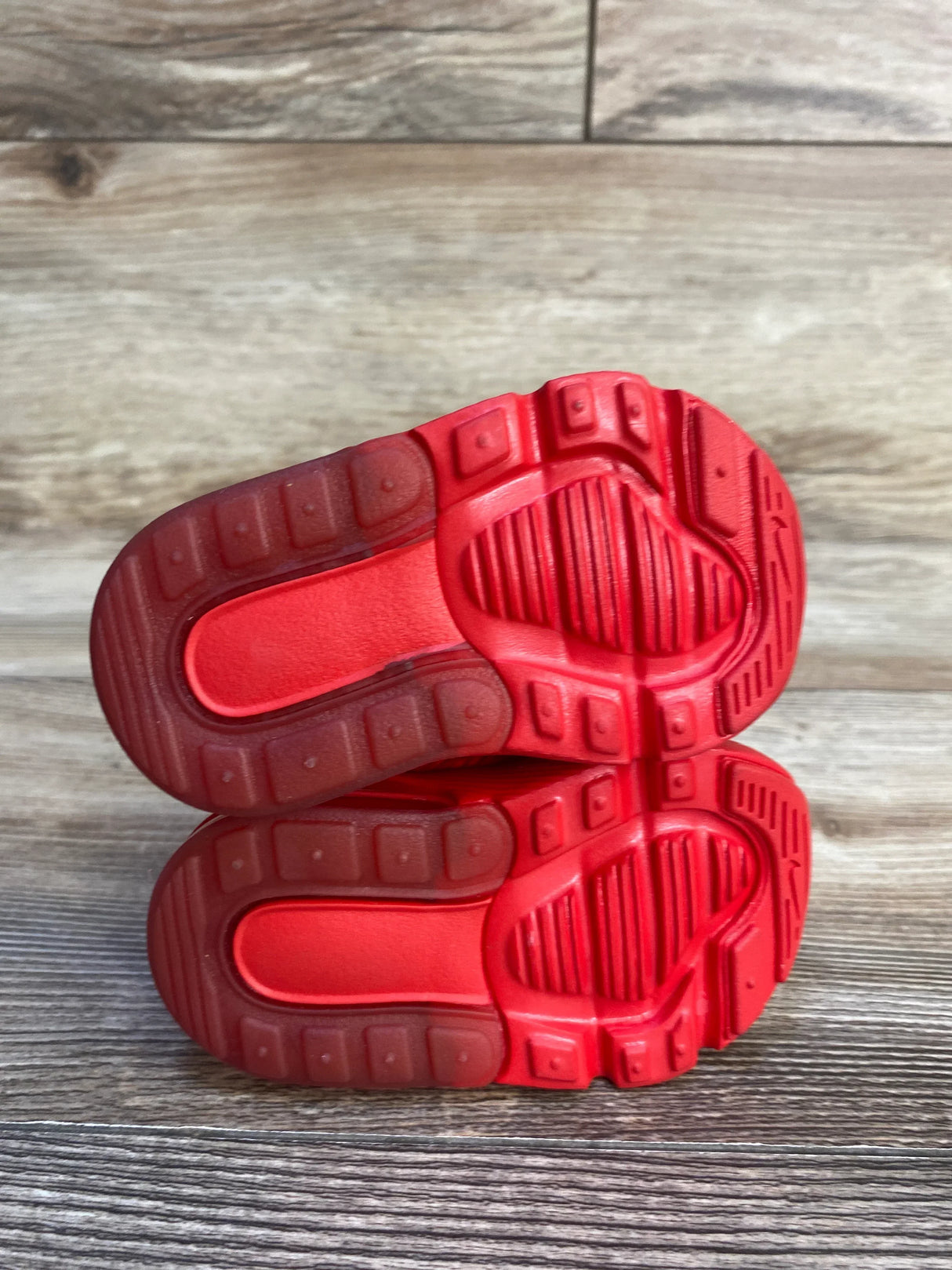 Red rubber soles of toddler sneakers on wood floor, children's footwear detail