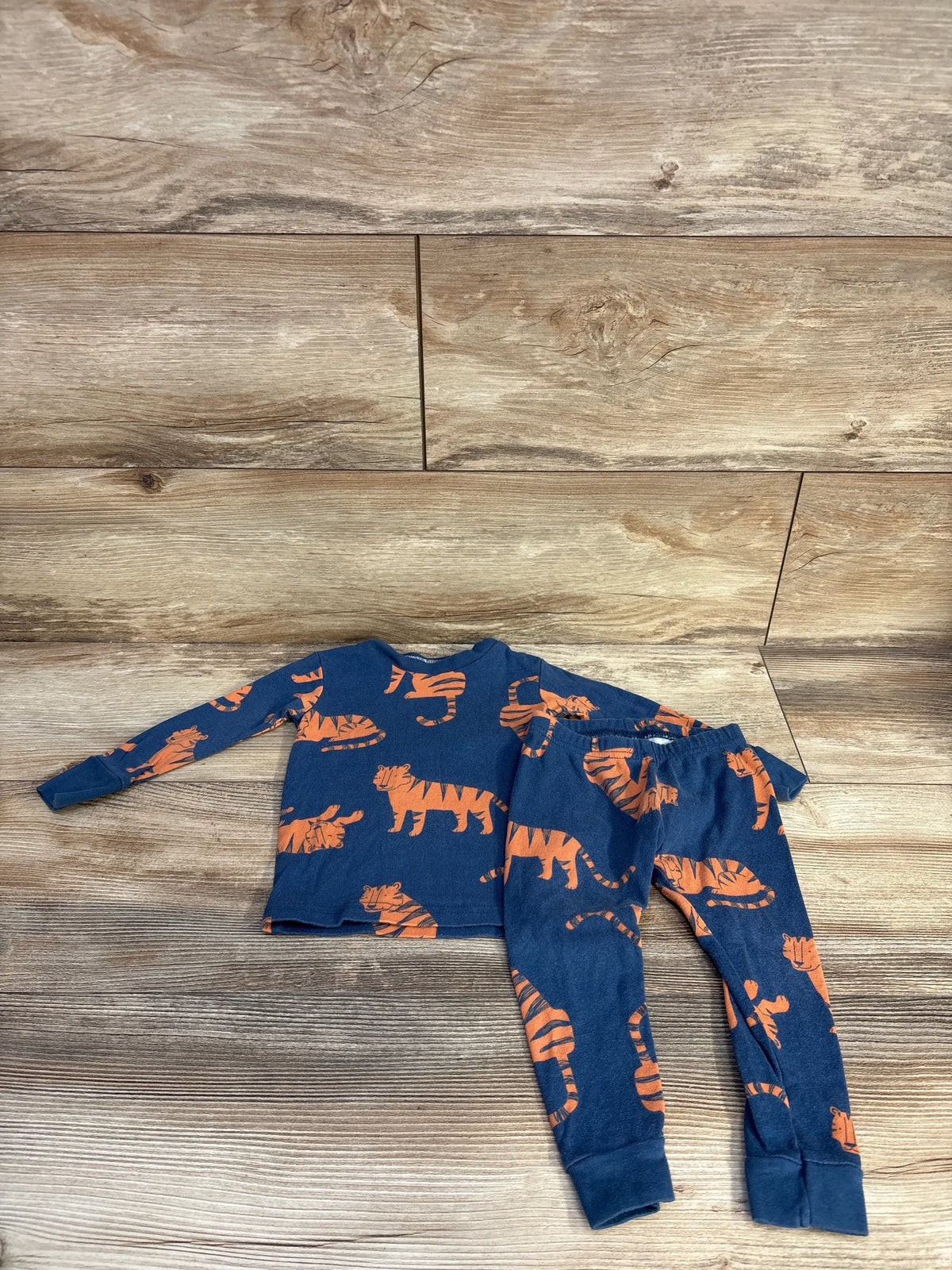 Just One You 2pc blue tiger print pajama set for baby size 12m on a wood background