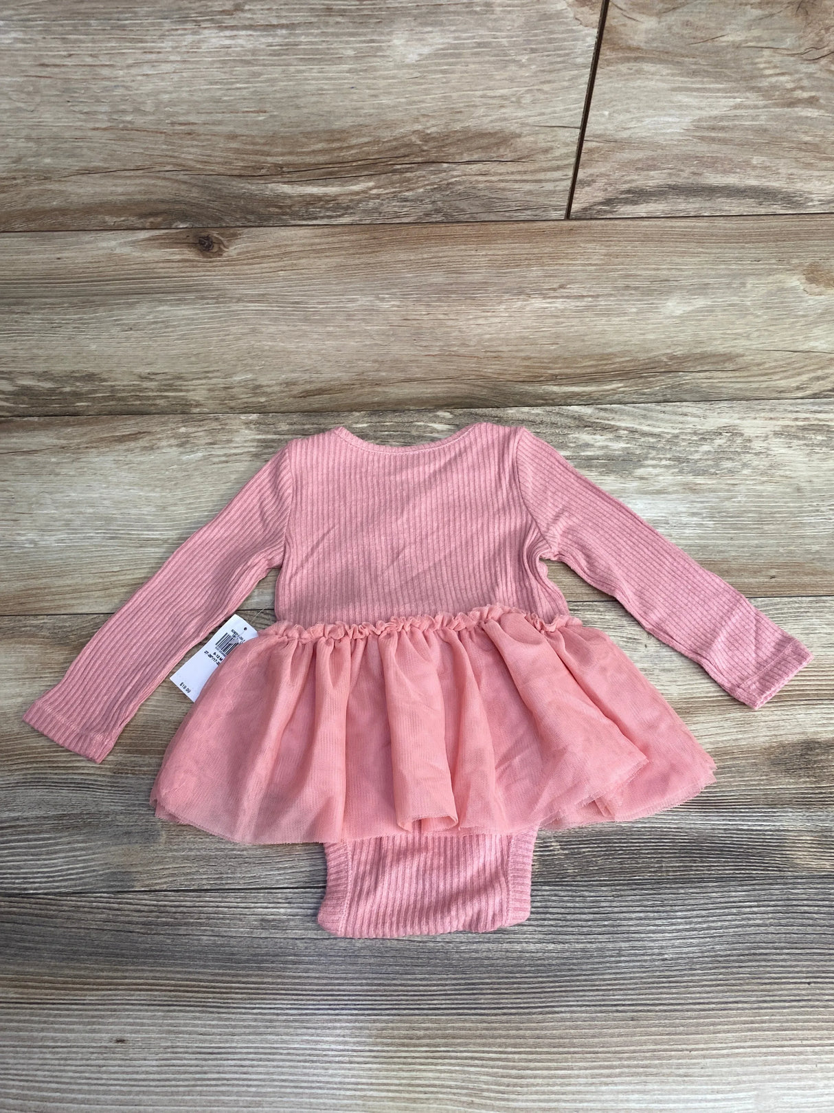Pink ribbed long-sleeve baby dress with tulle skirt laid on wooden floor, children's resale clothing