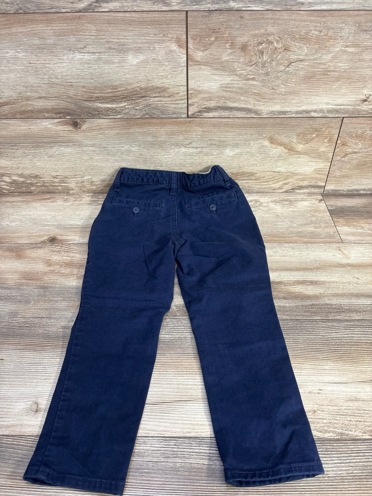 Rear view of Gap Kids navy classic chino pants size 5T showing back buttoned welt pockets and elasticized waistband on wood floor background
