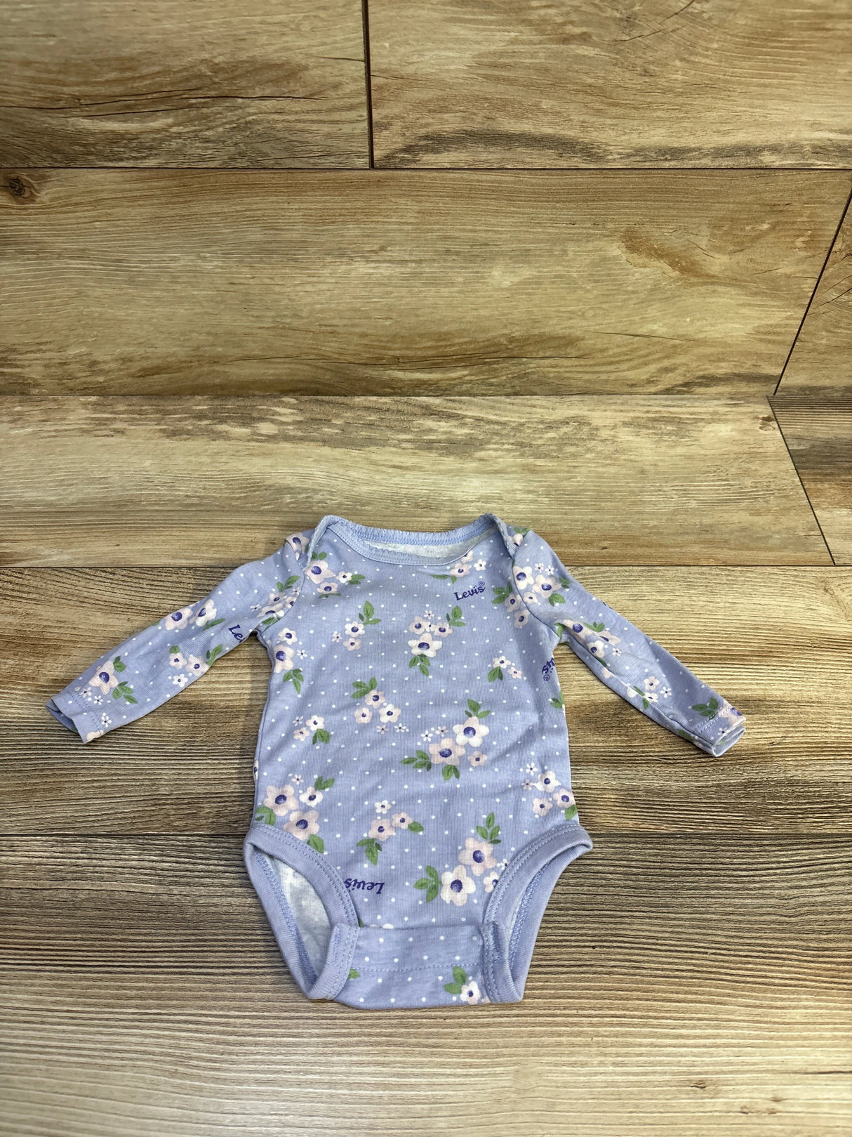 Flat lay of Levi’s lilac floral long-sleeve baby bodysuit size 3M showcasing flower print on wood background