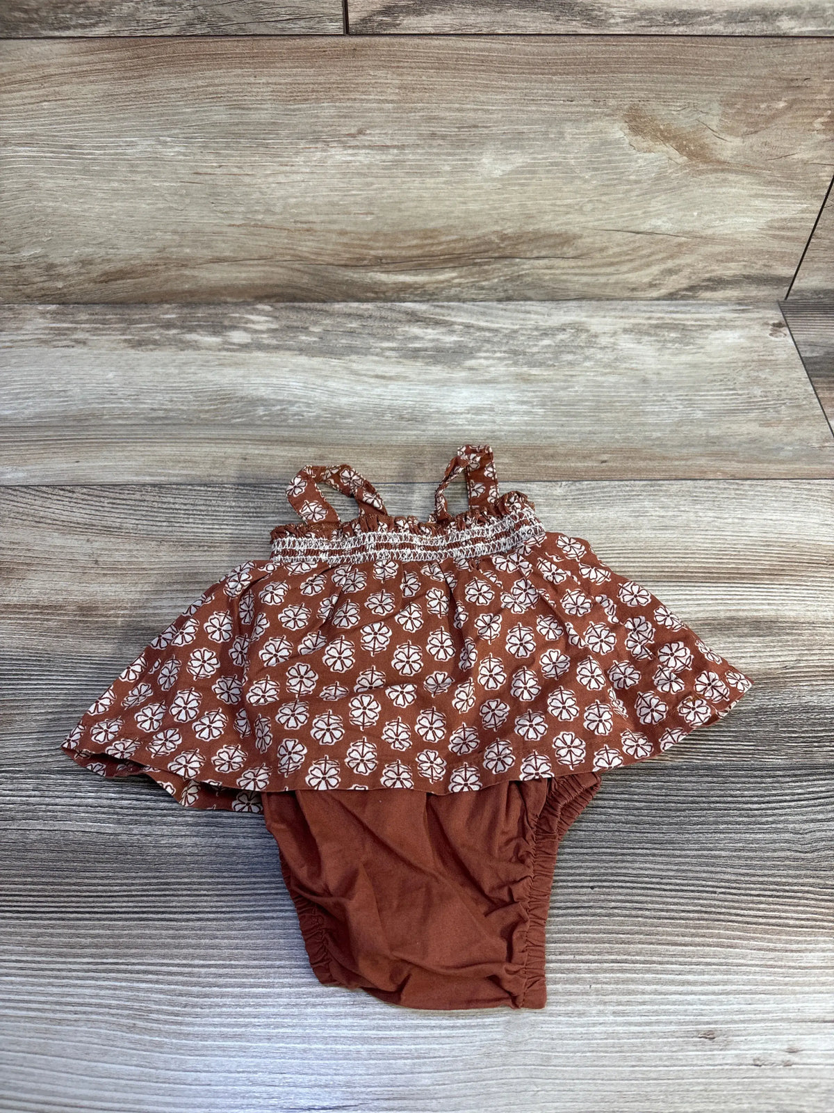 Top view of Just One You floral bodysuit dress in brown with floral print and shoulder straps on a wood surface