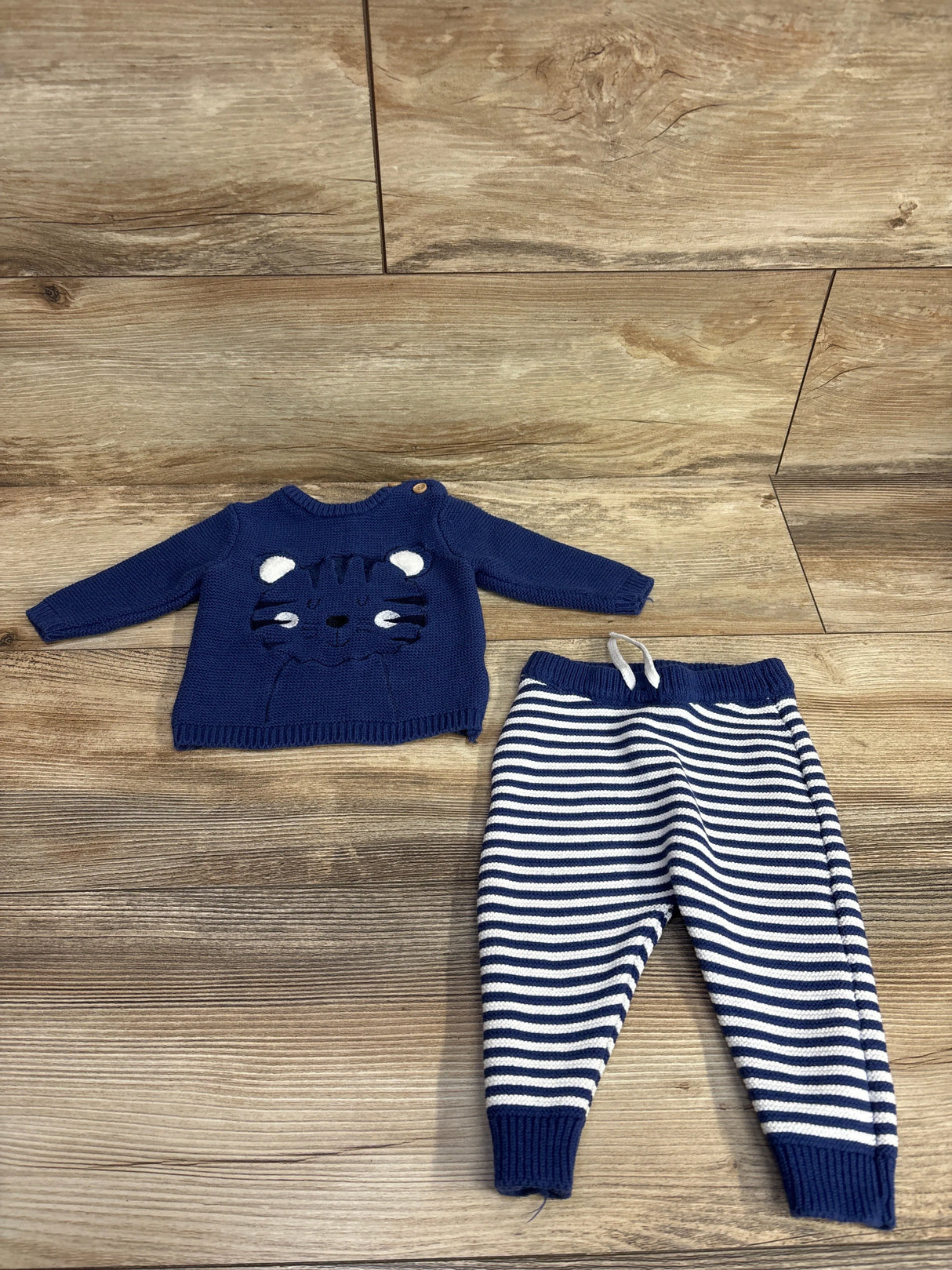 Navy blue baby sweater with tiger face and navy striped knit pants on wood floor
