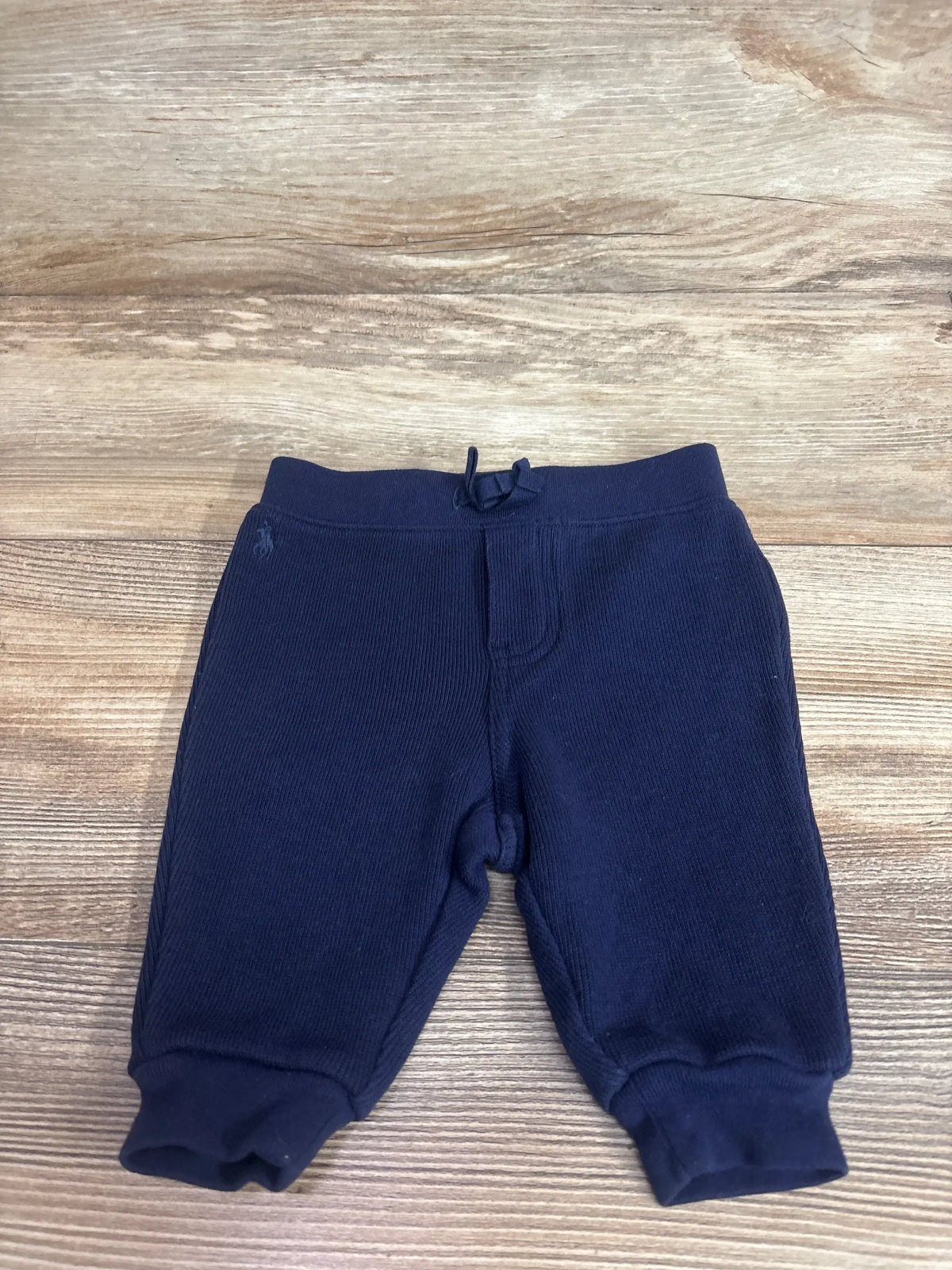 Flat lay of navy Ralph Lauren baby joggers, 3M, showing cuffed ankles, drawstring waistband and pony logo on wood background