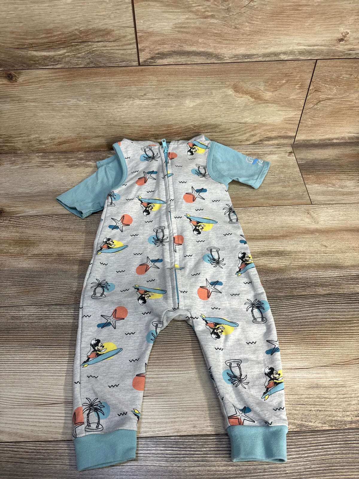 Front view of gray Disney Baby Mickey Mouse hooded zip-up jumpsuit with all-over beach print and blue cuffs on wood floor