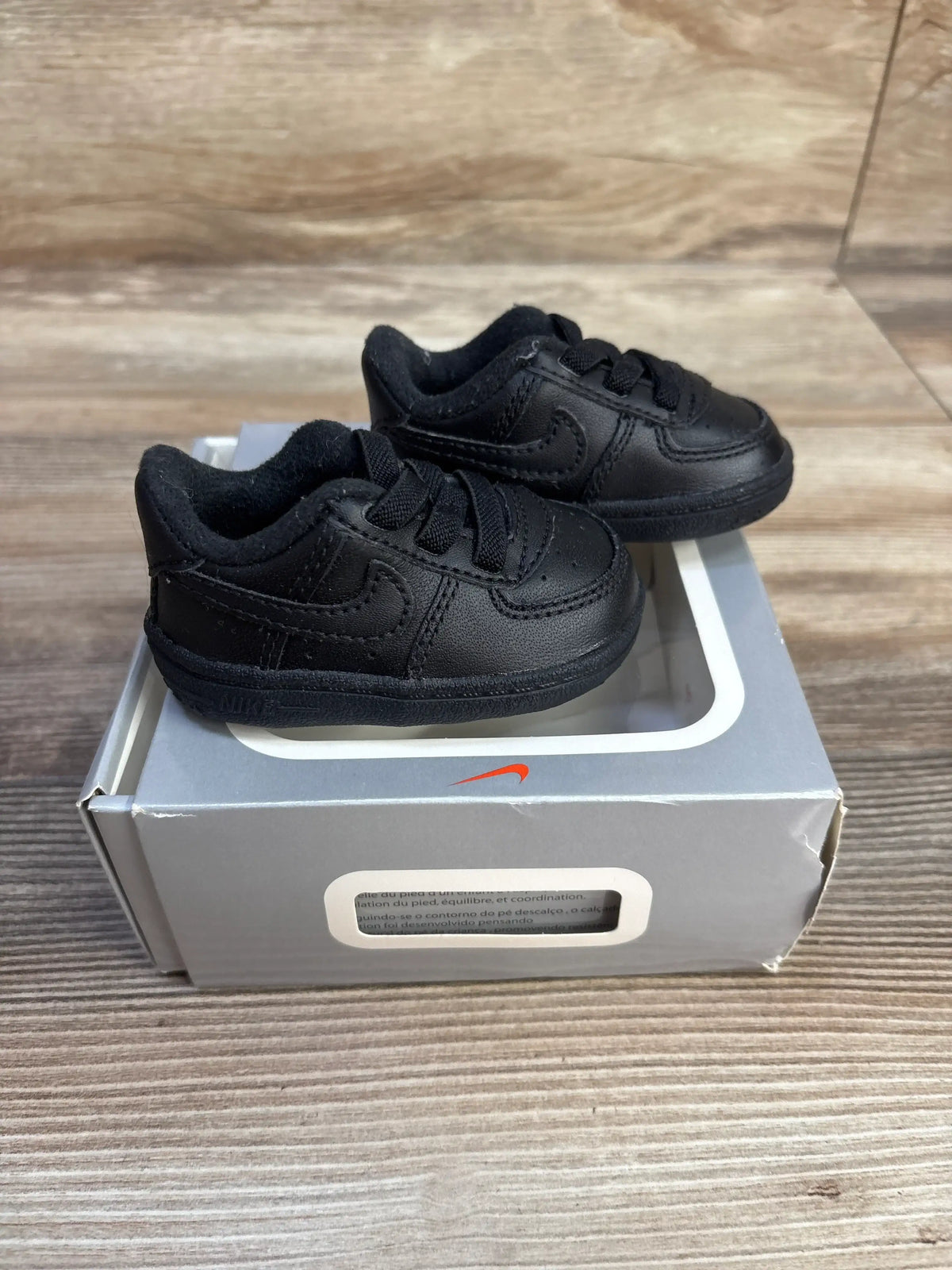 Front and side view of black Nike Air Force 1 crib shoes showcasing padded collars and lace closures on a silver shoebox