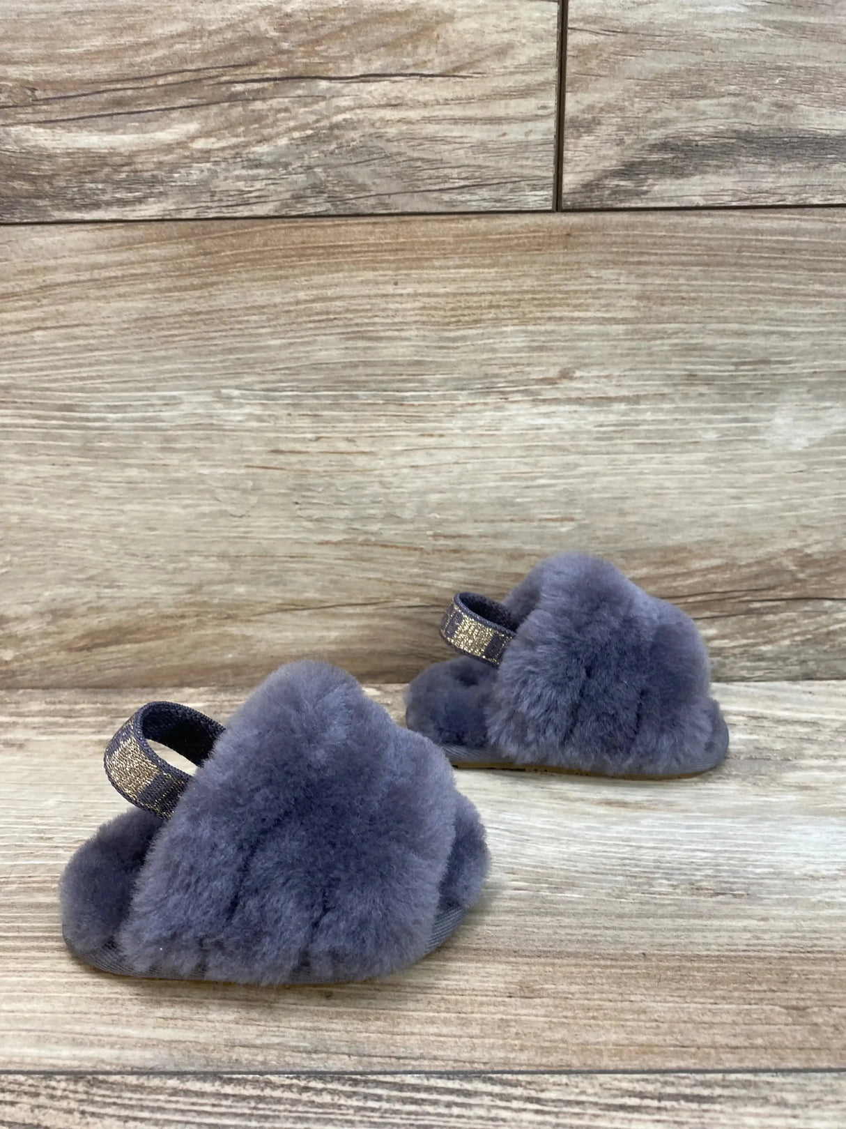 Angled front view of UGG Fluff Yeah toddler slides showing grey fluffy upper and glitter heel strap on wood background