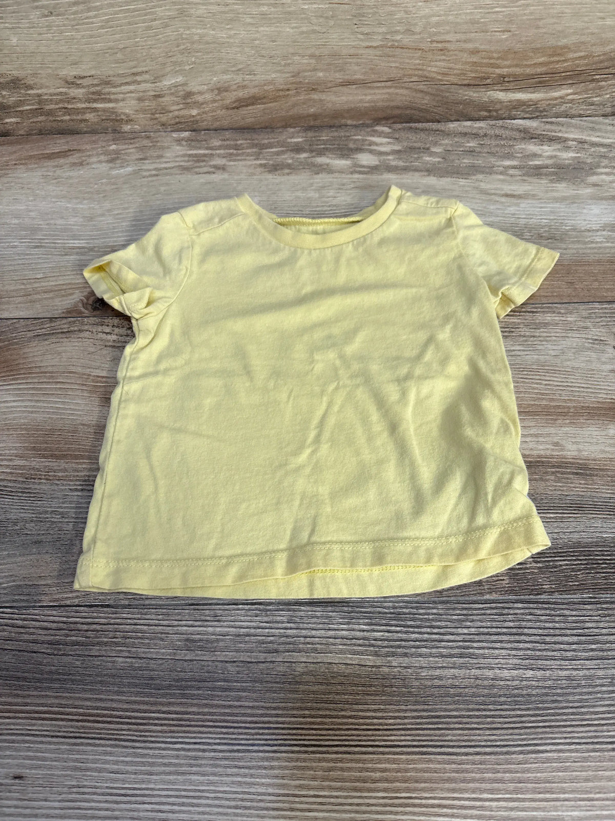 Front view of Honest Baby yellow shirt, size 3-6 months, showcasing short sleeves and crew neckline on wood background