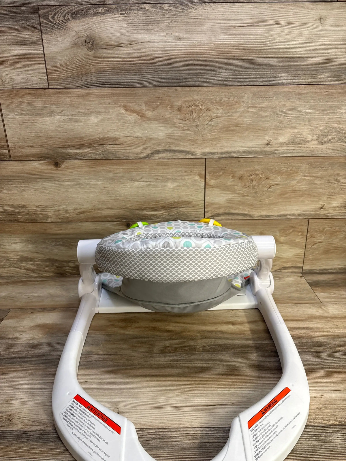 Front view of Fisher Price Sit-Me-Up floor seat showing starlight bursts cushion pattern and white plastic base on wood floor