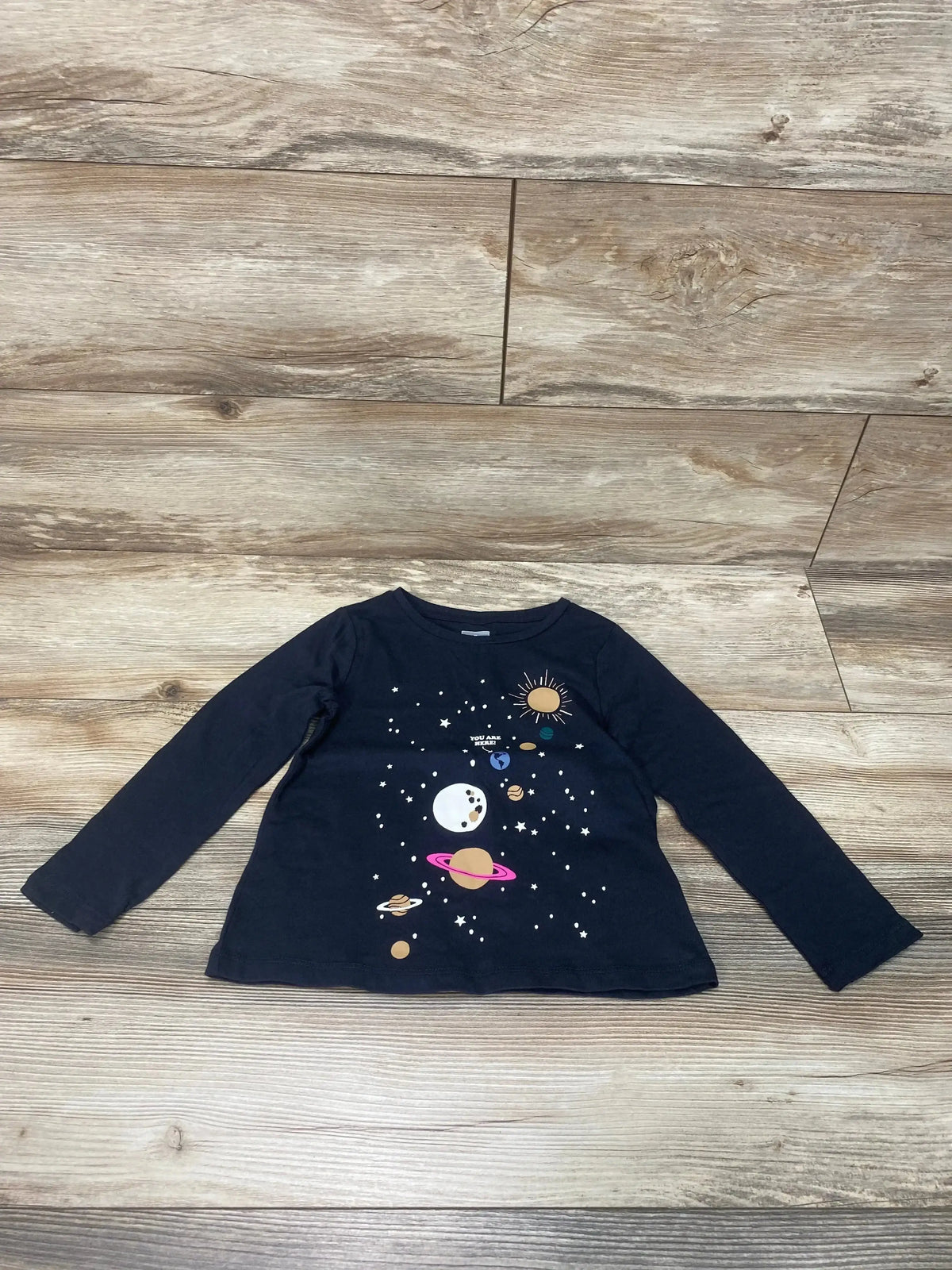 Front view of black Baby Gap toddler long-sleeve shirt showcasing colorful planet and you are here space graphic on light wood background