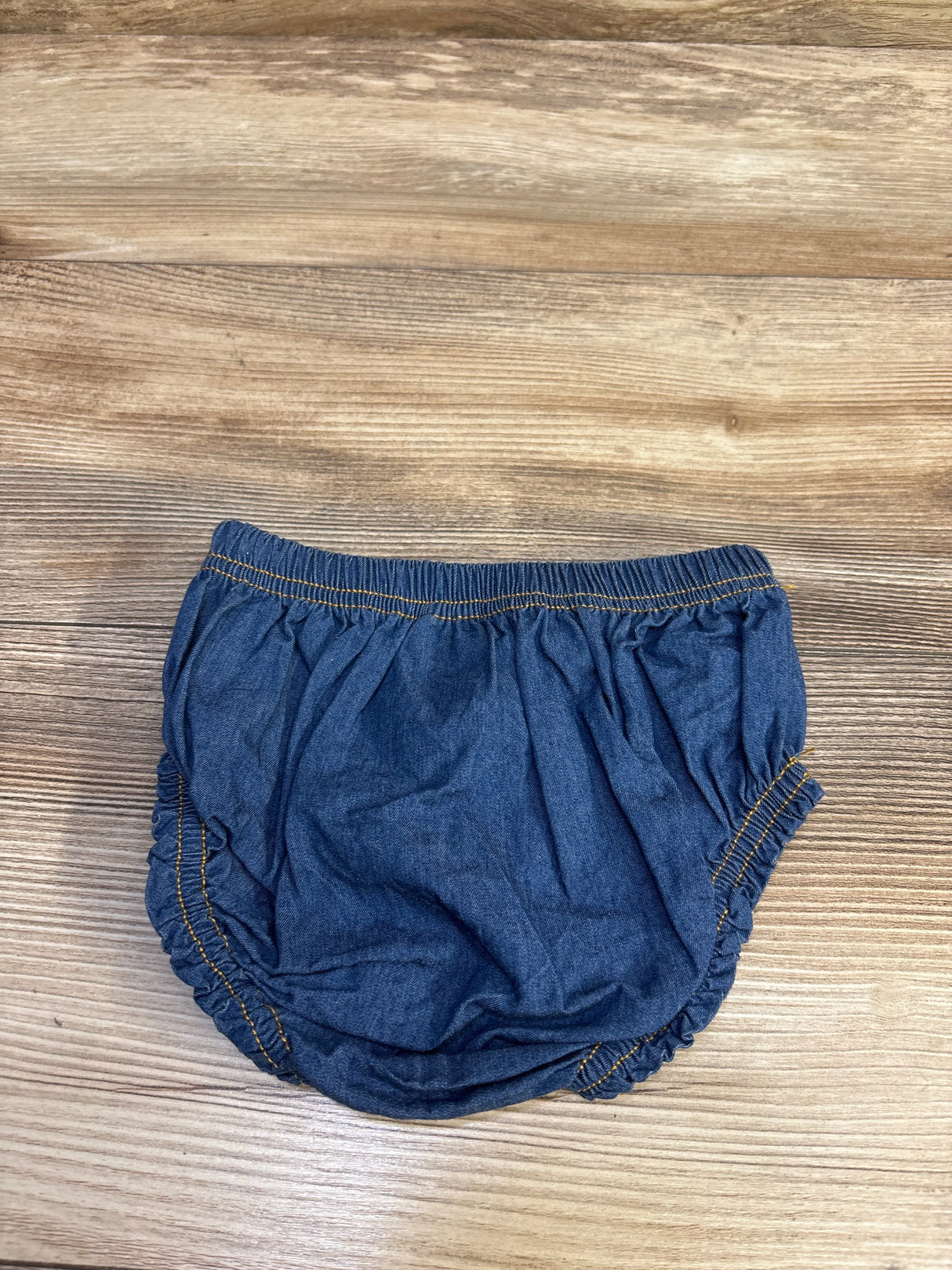 Top-down view of blue chambray bow bloomers showcasing elastic waistband and gathered leg openings on a light wood surface